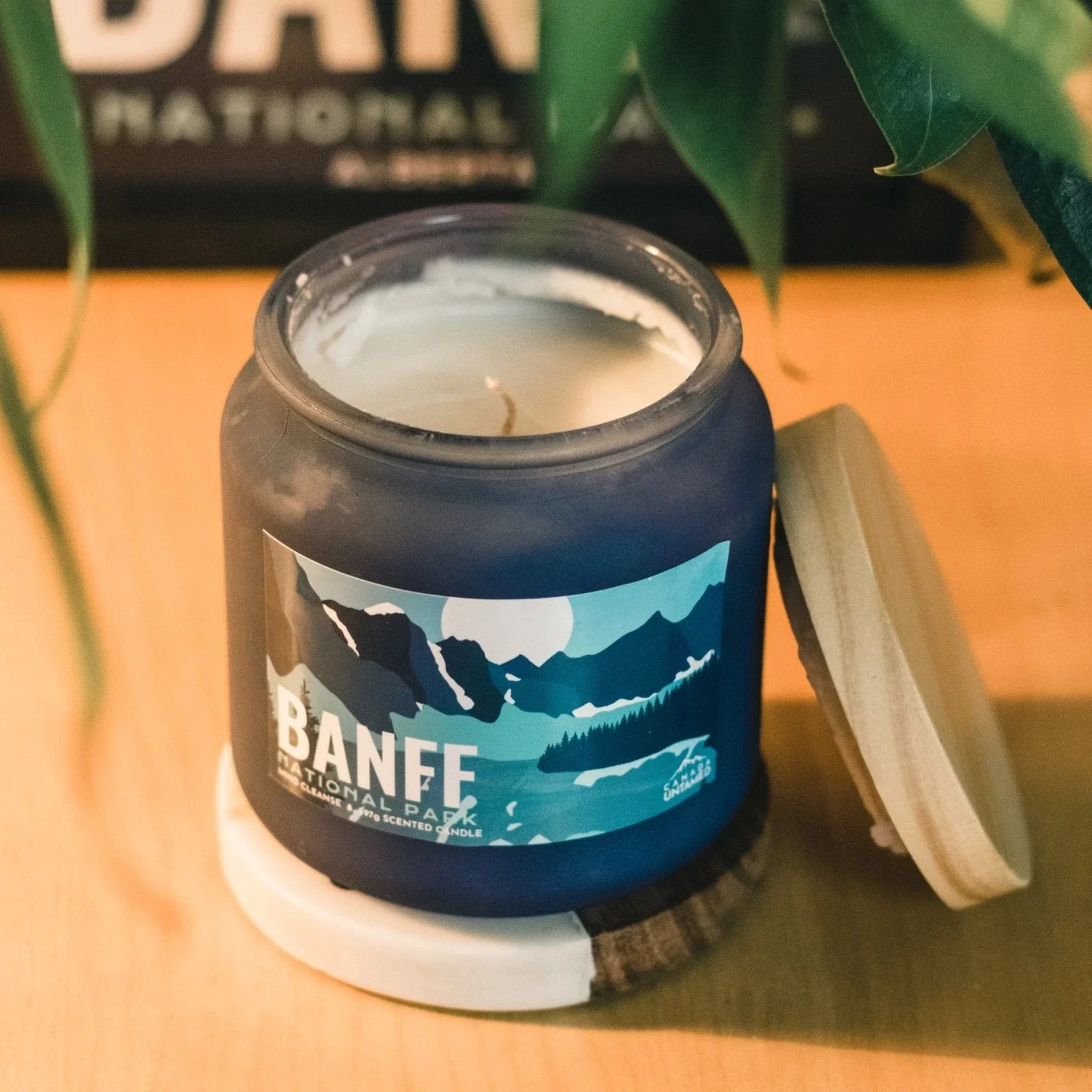 Banff National Park blue glass scented candle with mountain label on wooden table