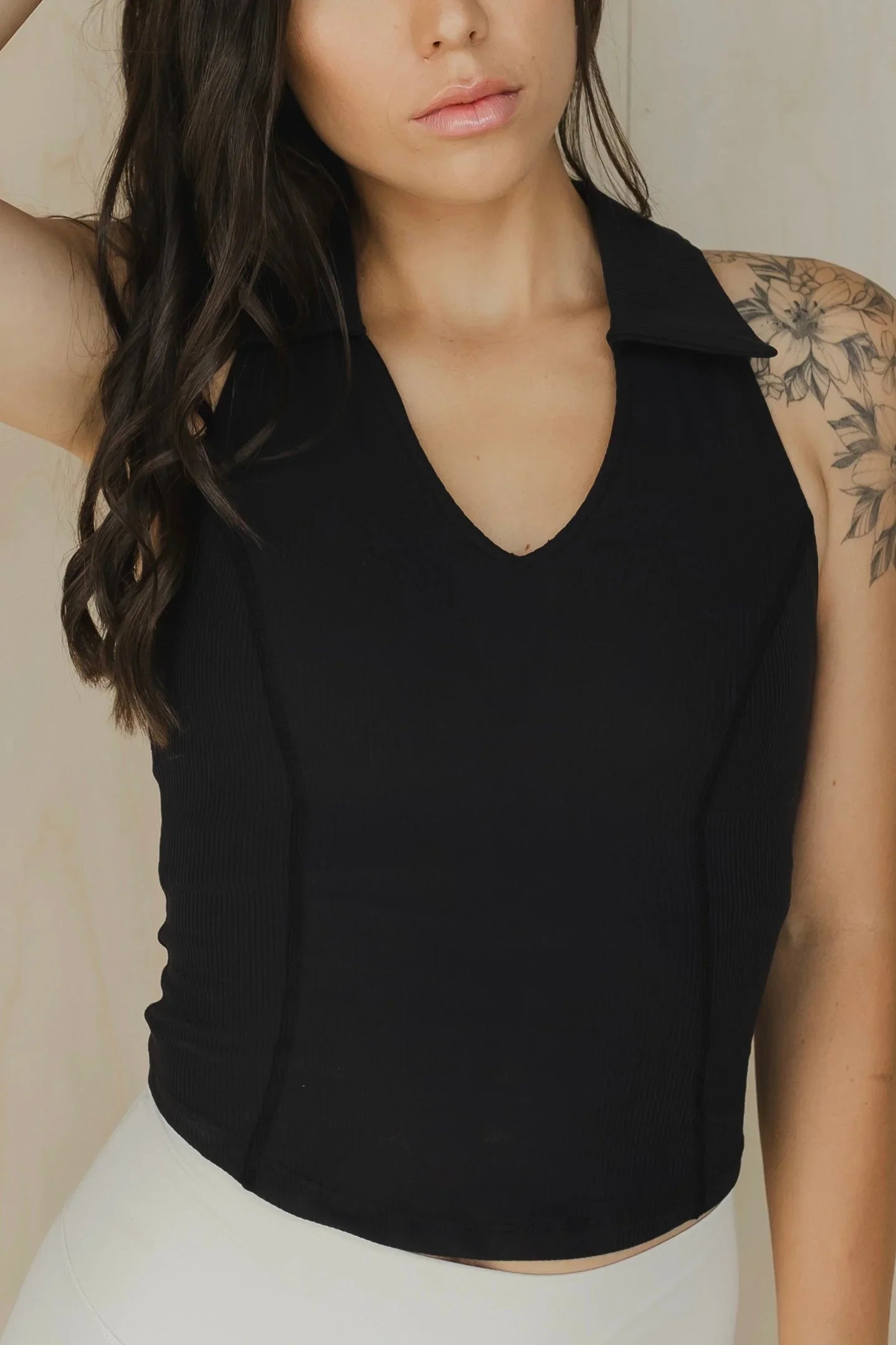 Woman in sleeveless black collared top with floral shoulder tattoo, neutral background