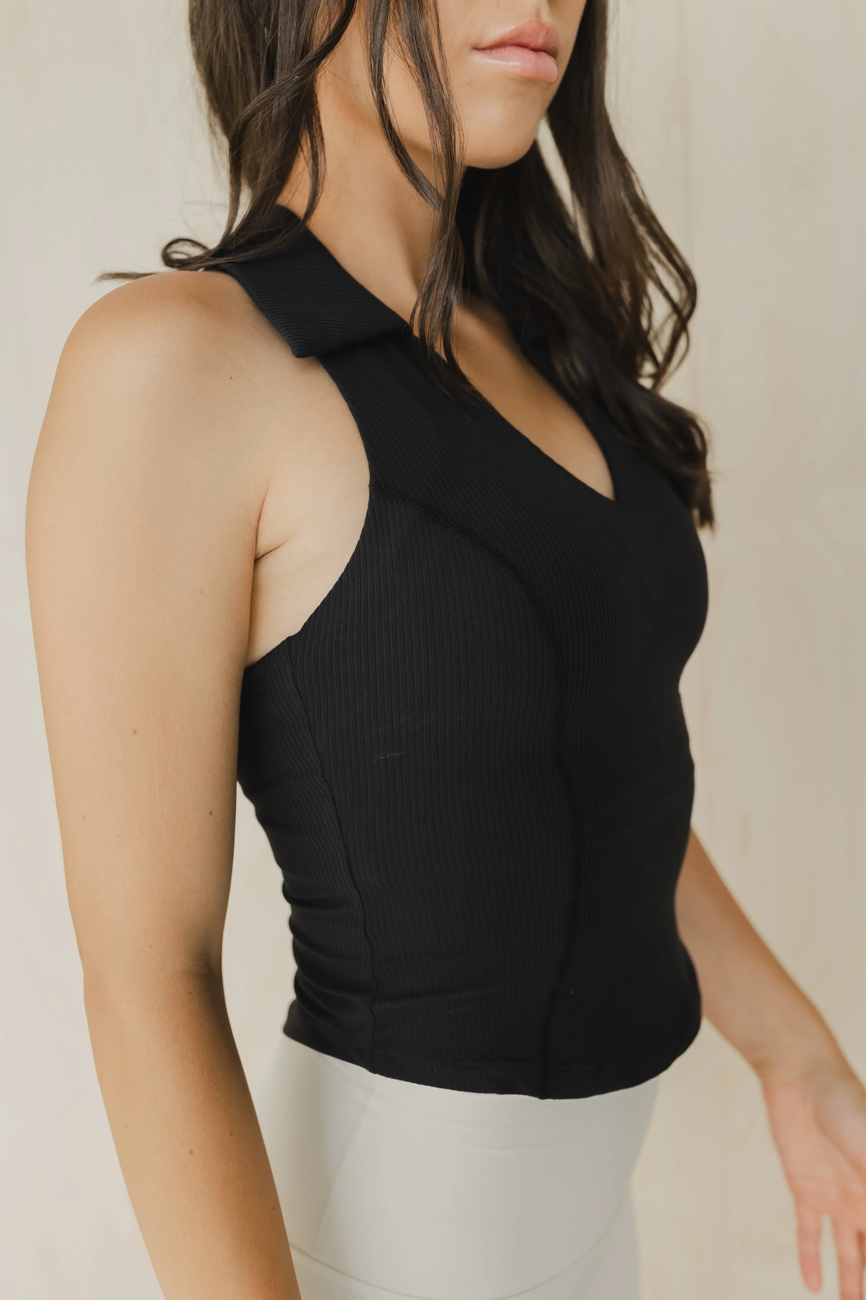 Woman wearing a fitted ribbed black sleeveless top with collar, neutral background