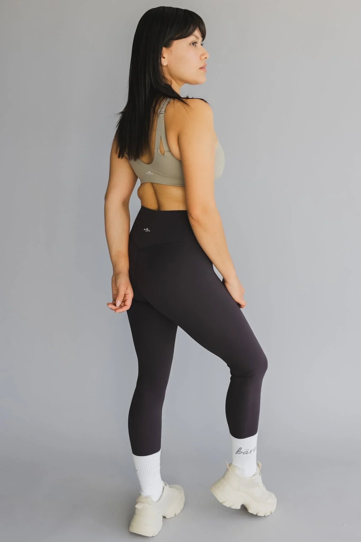 Woman in activewear posing in taupe sports bra, black leggings, white socks, chunky sneakers