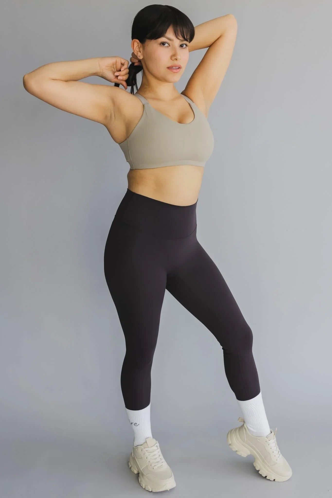 Woman modeling beige sports bra and black high waisted leggings with chunky sneakers