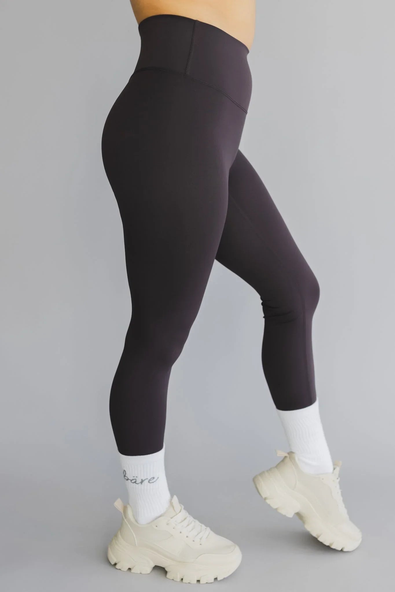 Black high-waisted leggings with white socks and chunky white sneakers on gray background