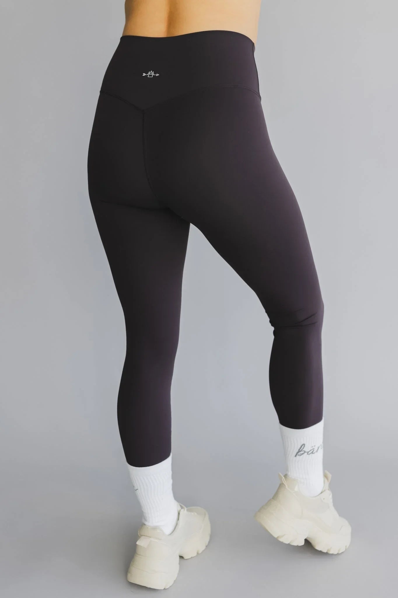 High-waisted black leggings, white socks, chunky sneakers on person with gray background