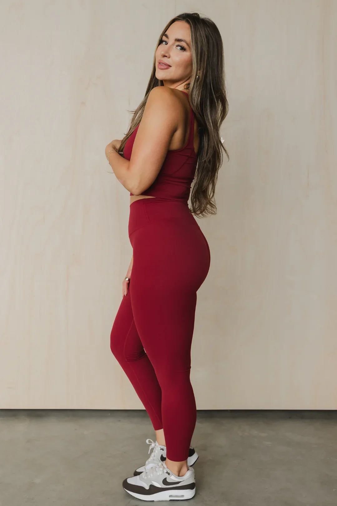 Woman in maroon athletic leggings and top posing sideways on concrete floor