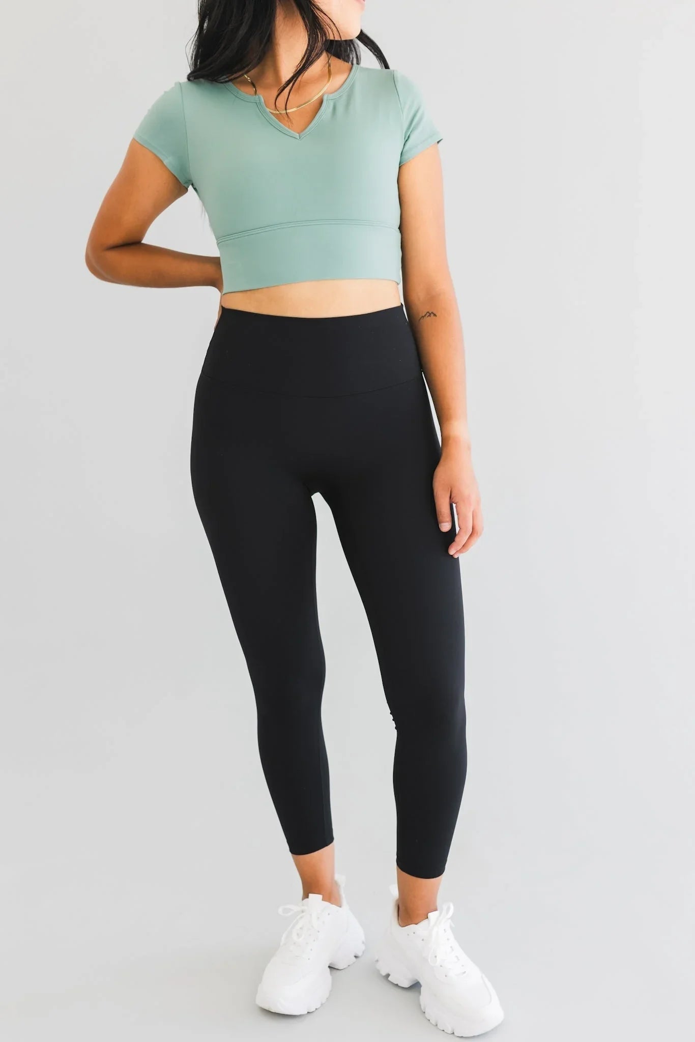 Woman wearing black high-waisted leggings and mint green crop top with white sneakers