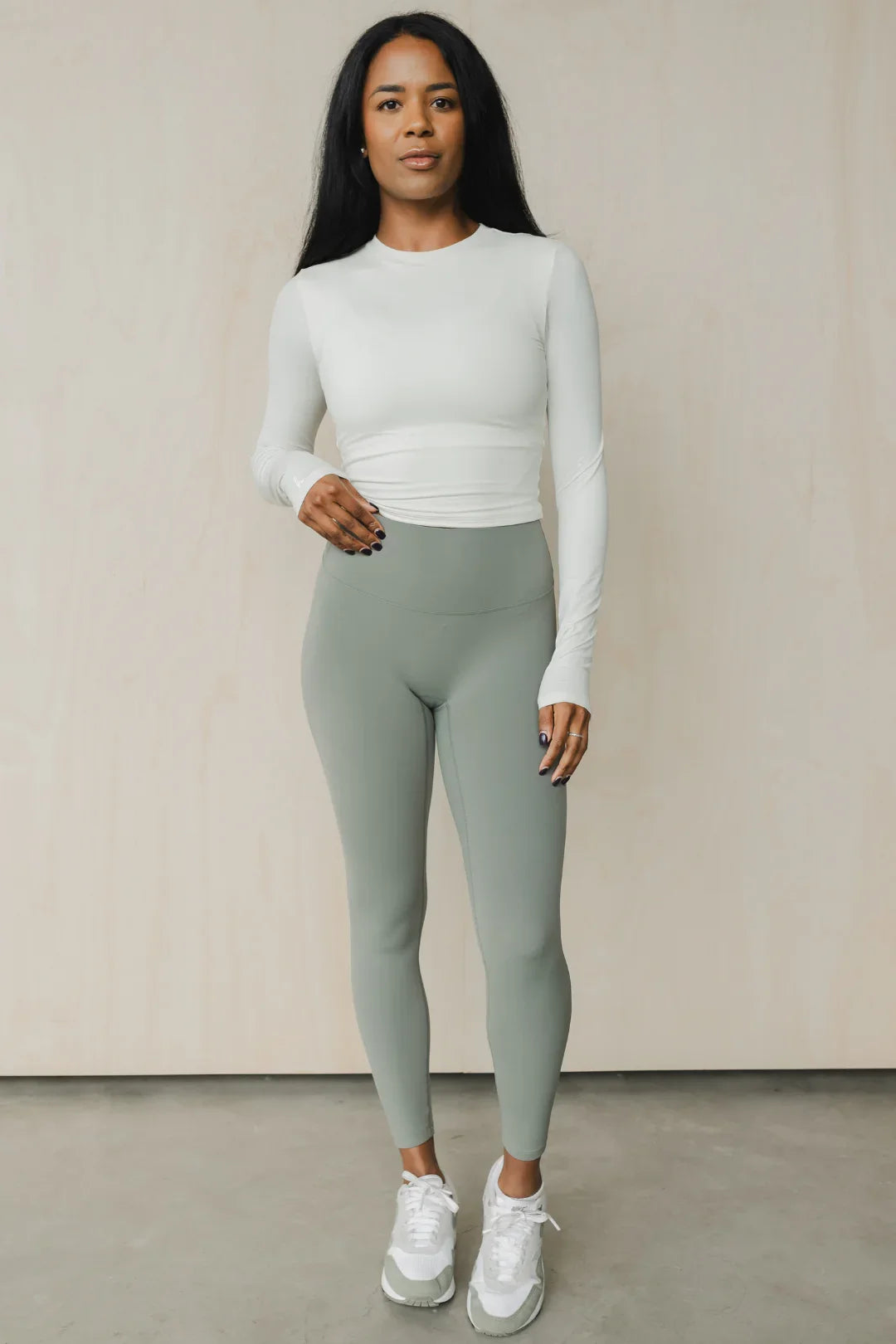 Woman wearing light grey long sleeve top, sage green leggings, and white sneakers