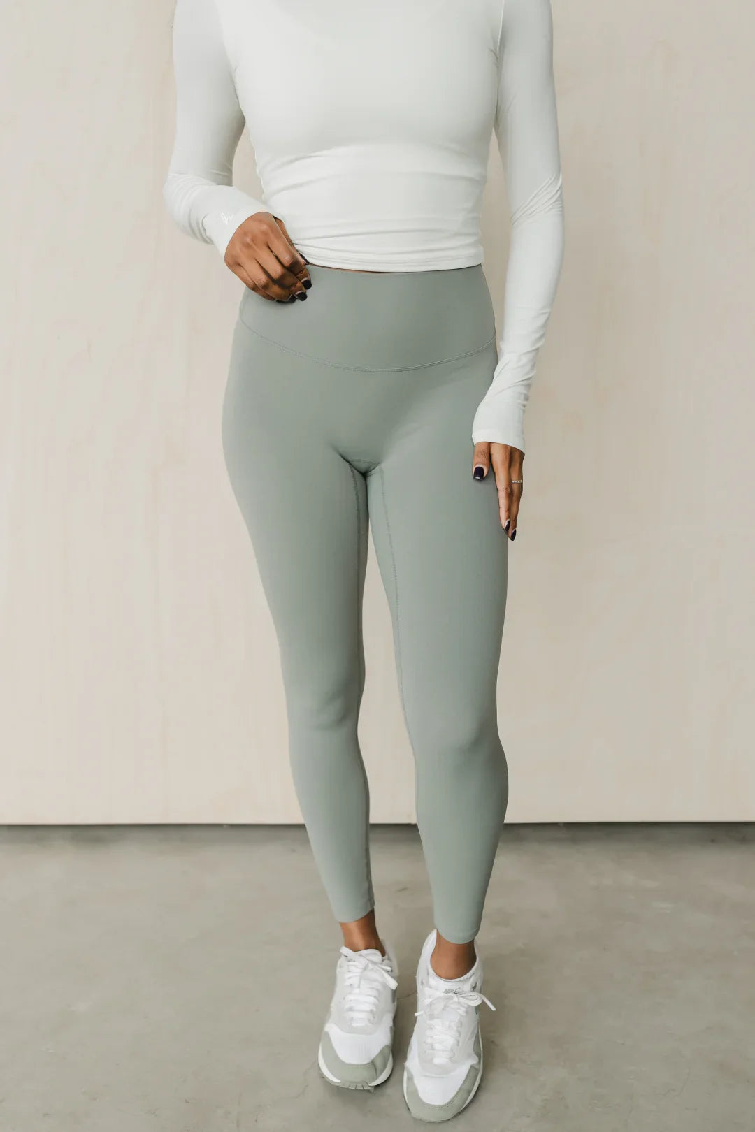 Woman in sage green high-waisted leggings, white long-sleeve top, and white sneakers