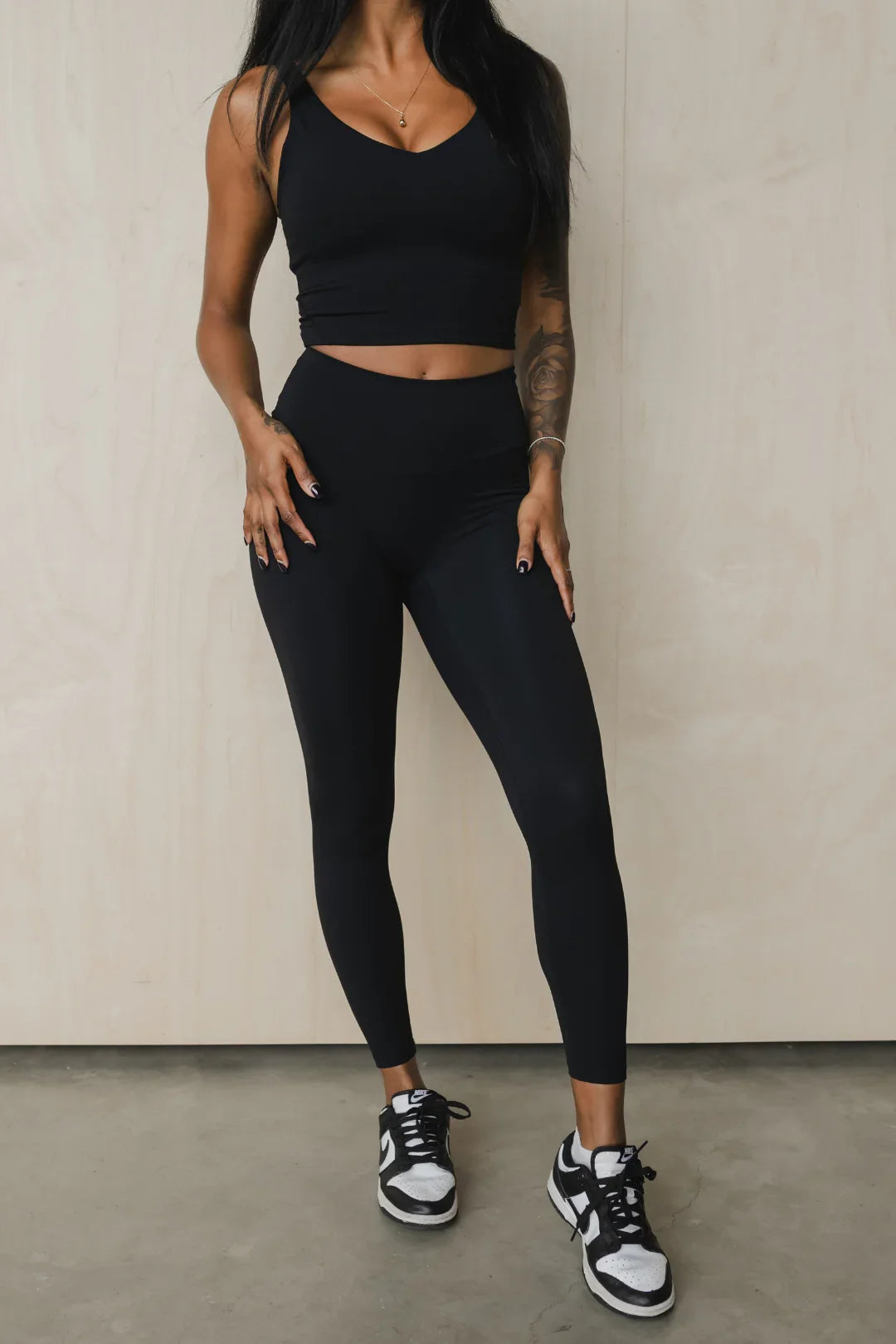 Woman wearing black workout set with leggings and crop top, black and white sneakers
