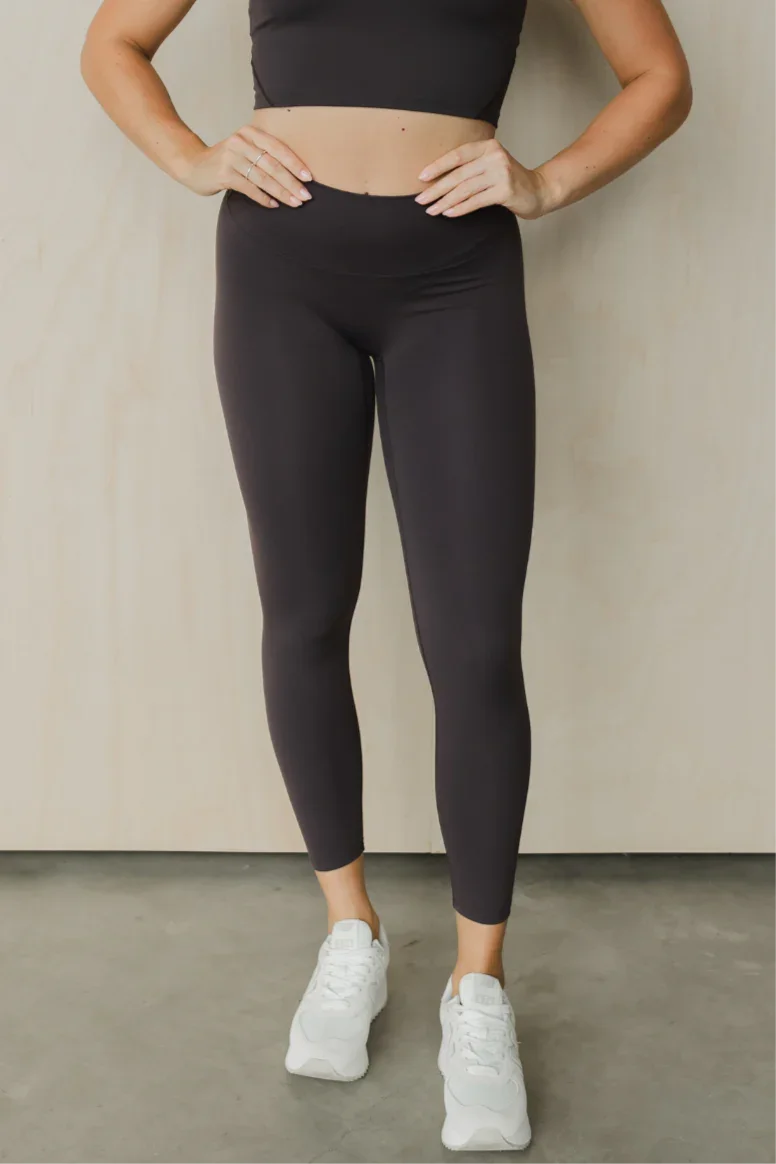 Woman wearing black high-waisted leggings and white sneakers standing indoors