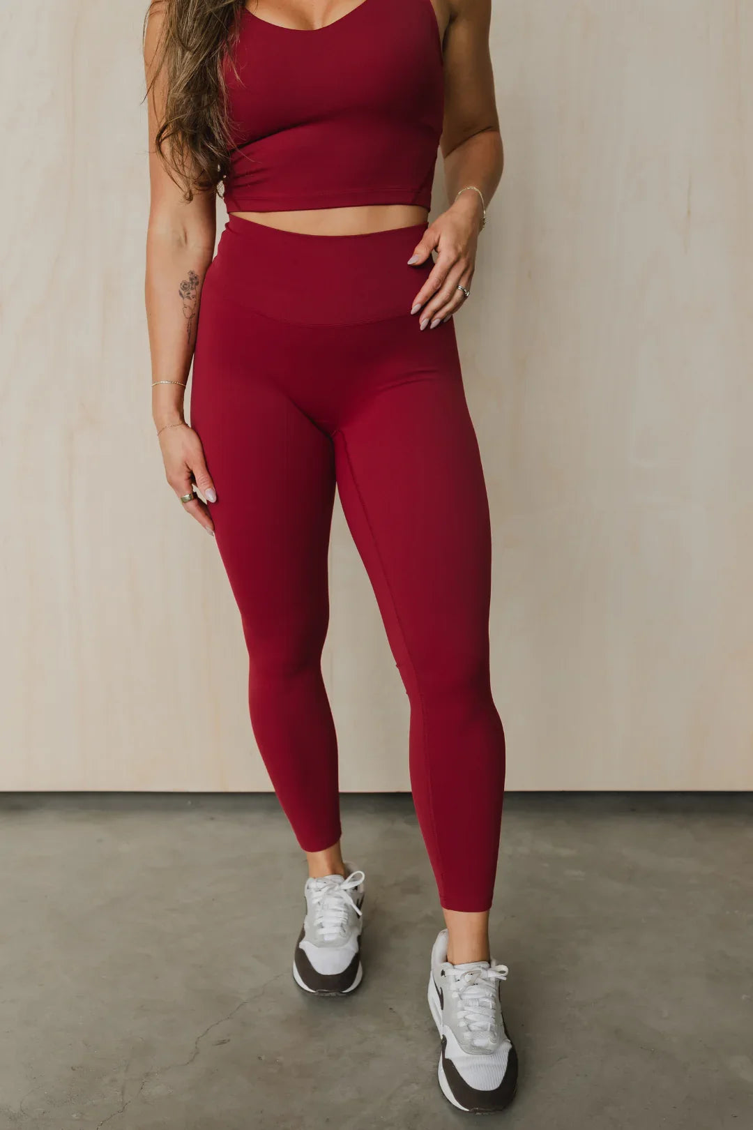 Woman in burgundy workout leggings and crop top, athletic wear, standing on concrete floor