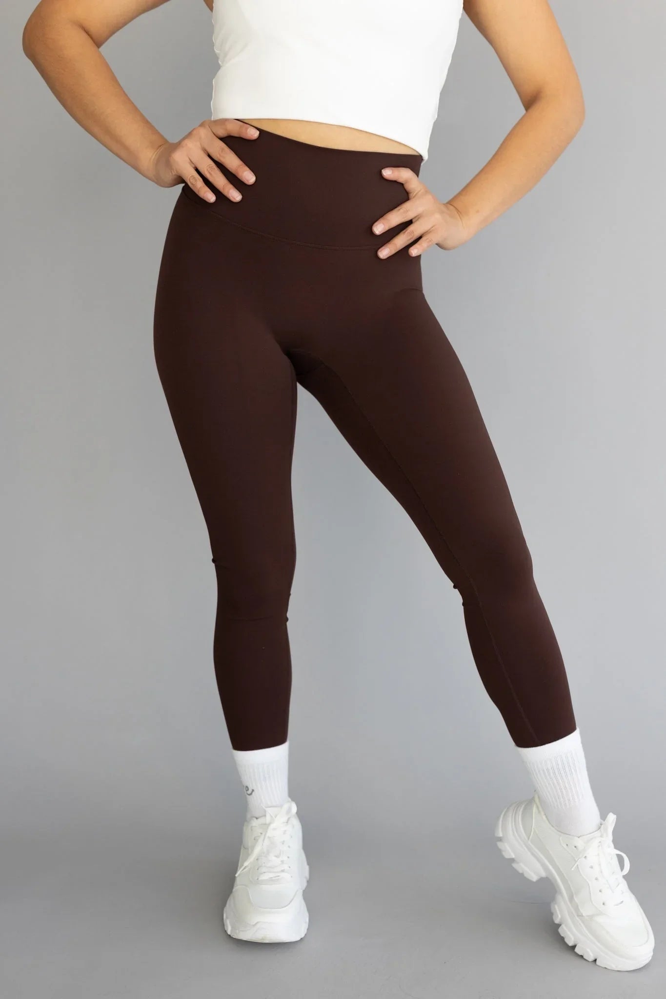 Woman wearing high-waisted brown leggings, white crop top, and white sneakers