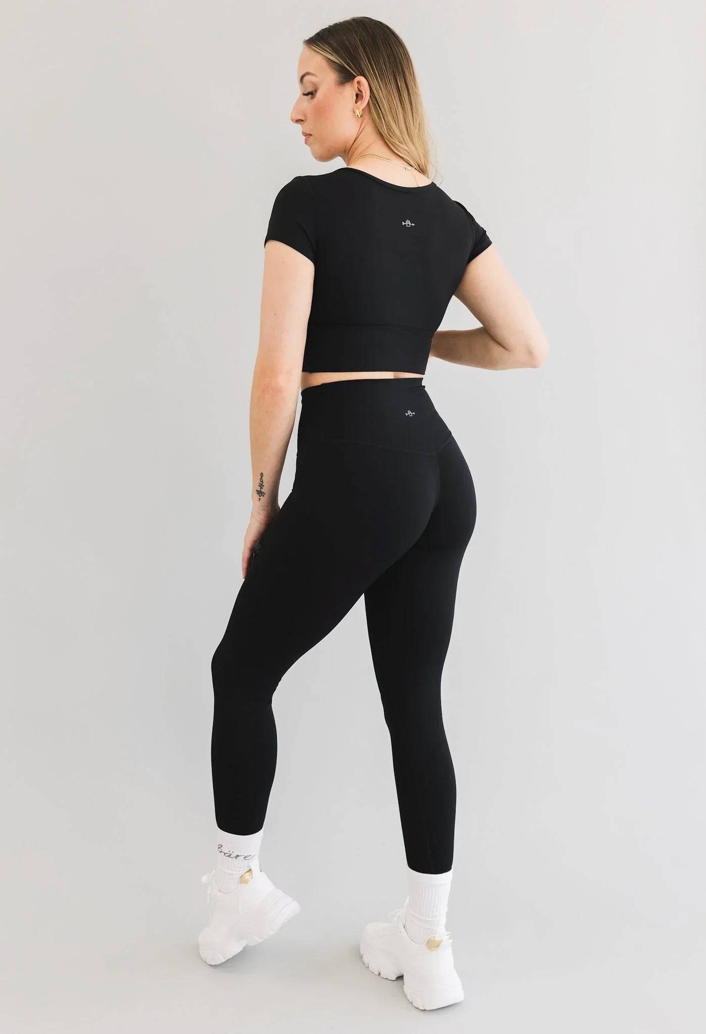 Woman in black activewear set, high-waisted leggings and crop top, white chunky sneakers