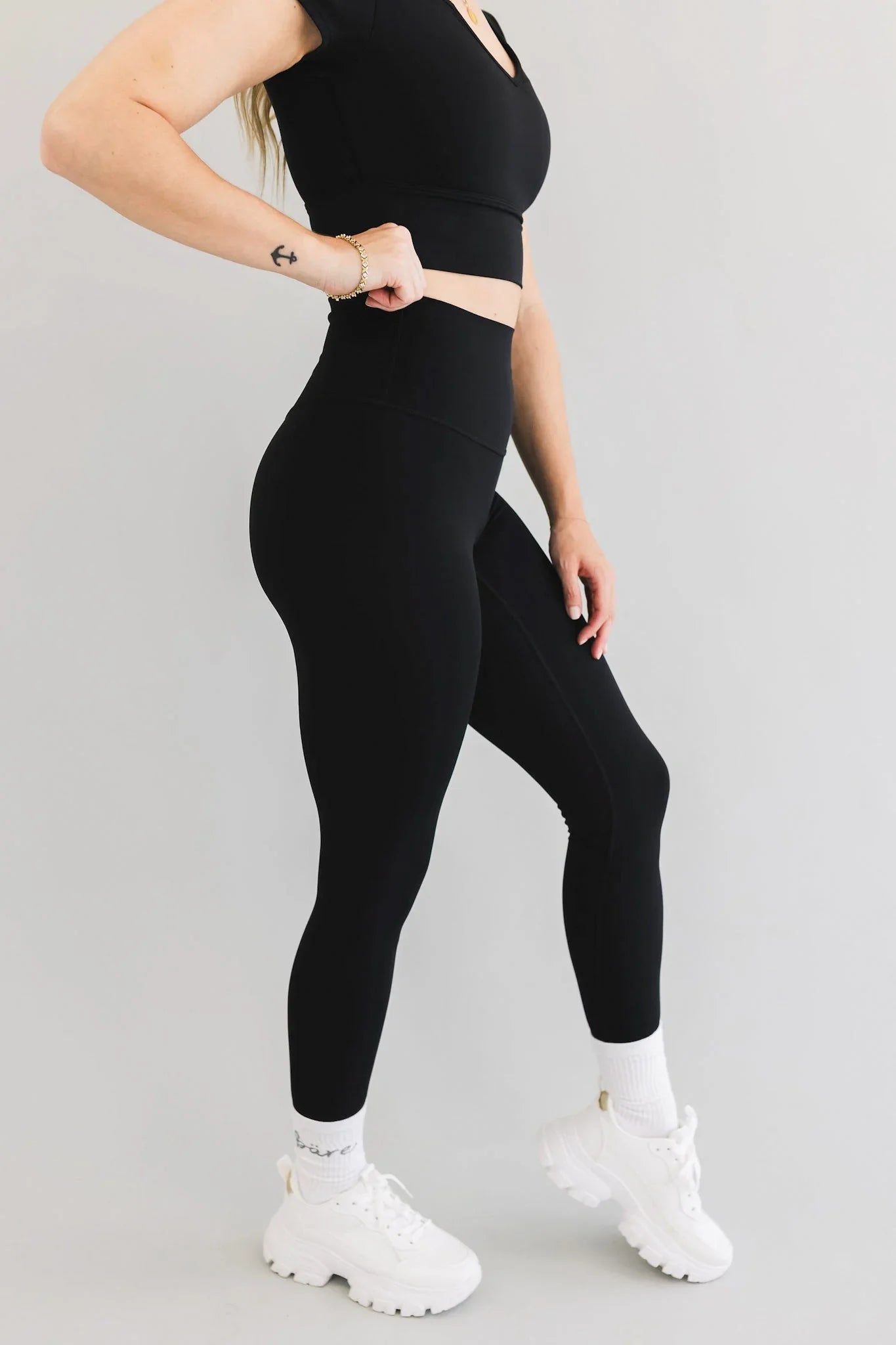 Woman in black high-waisted leggings and crop top with white chunky sneakers