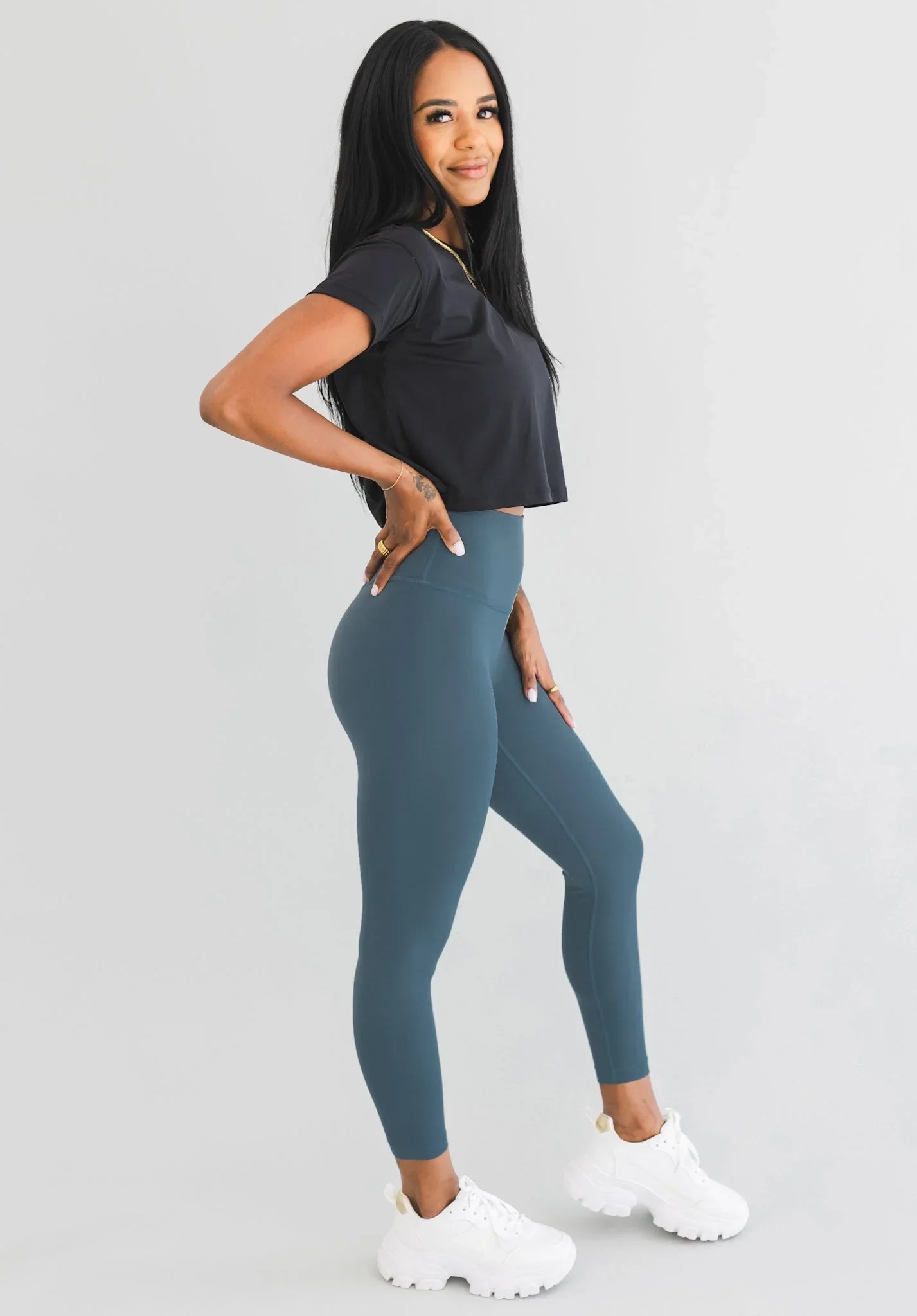 Woman modeling teal high-waisted leggings, black crop top, and white sneakers