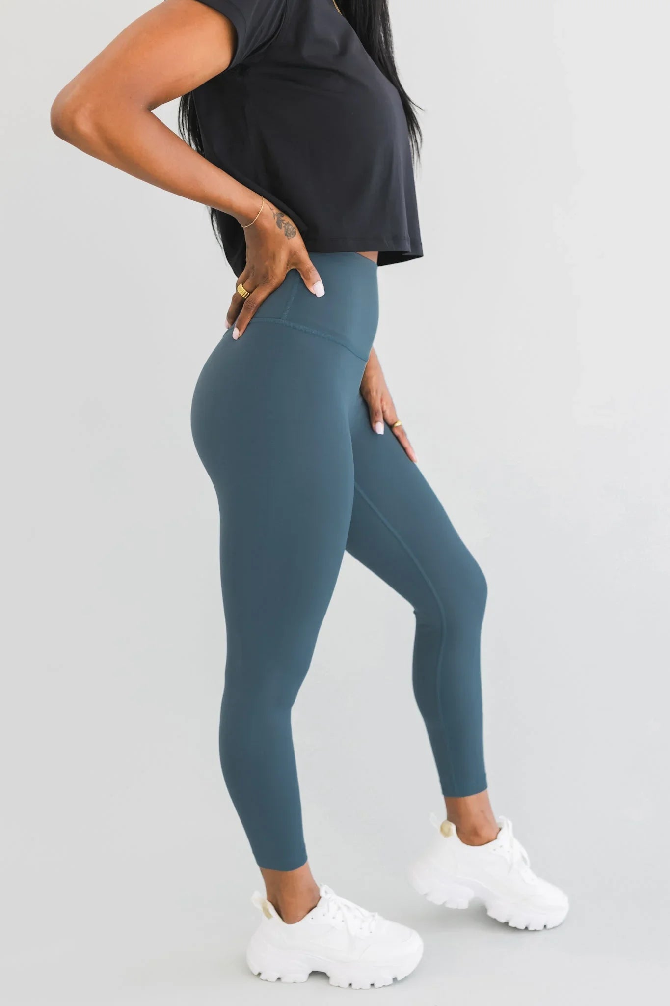Woman modeling high-waisted blue leggings and white sneakers, black cropped top