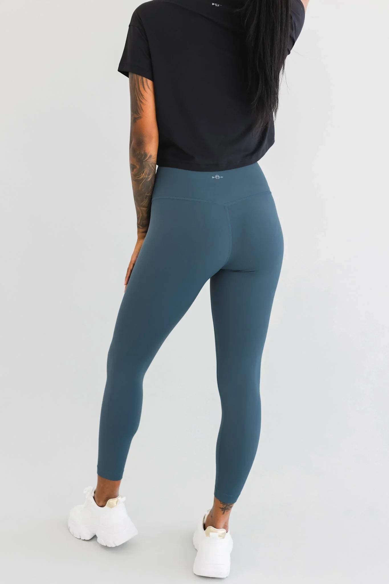 Woman modeling high-waisted blue leggings, black crop top, and white chunky sneakers