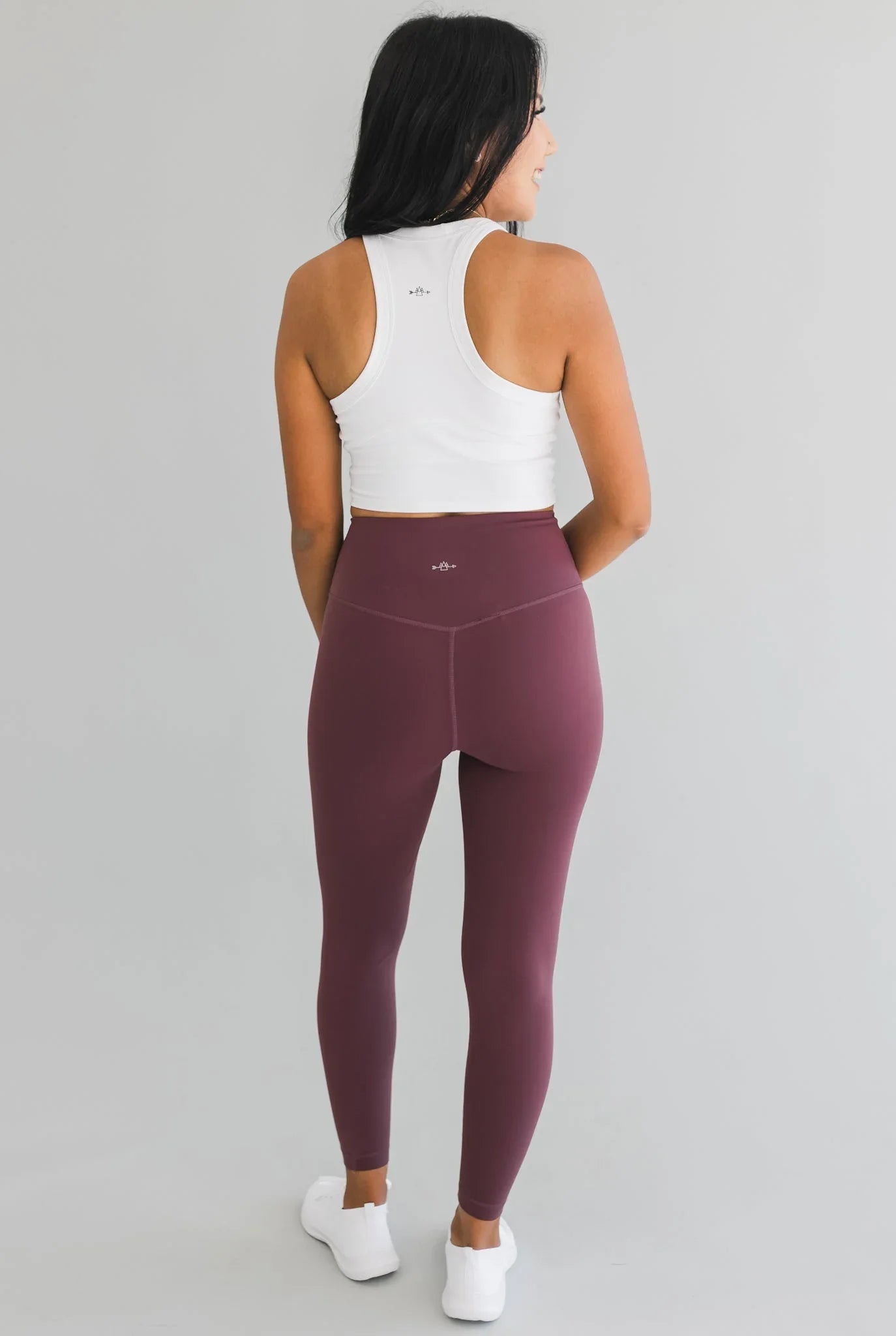 Woman in burgundy high-waisted leggings and white crop top on gray background