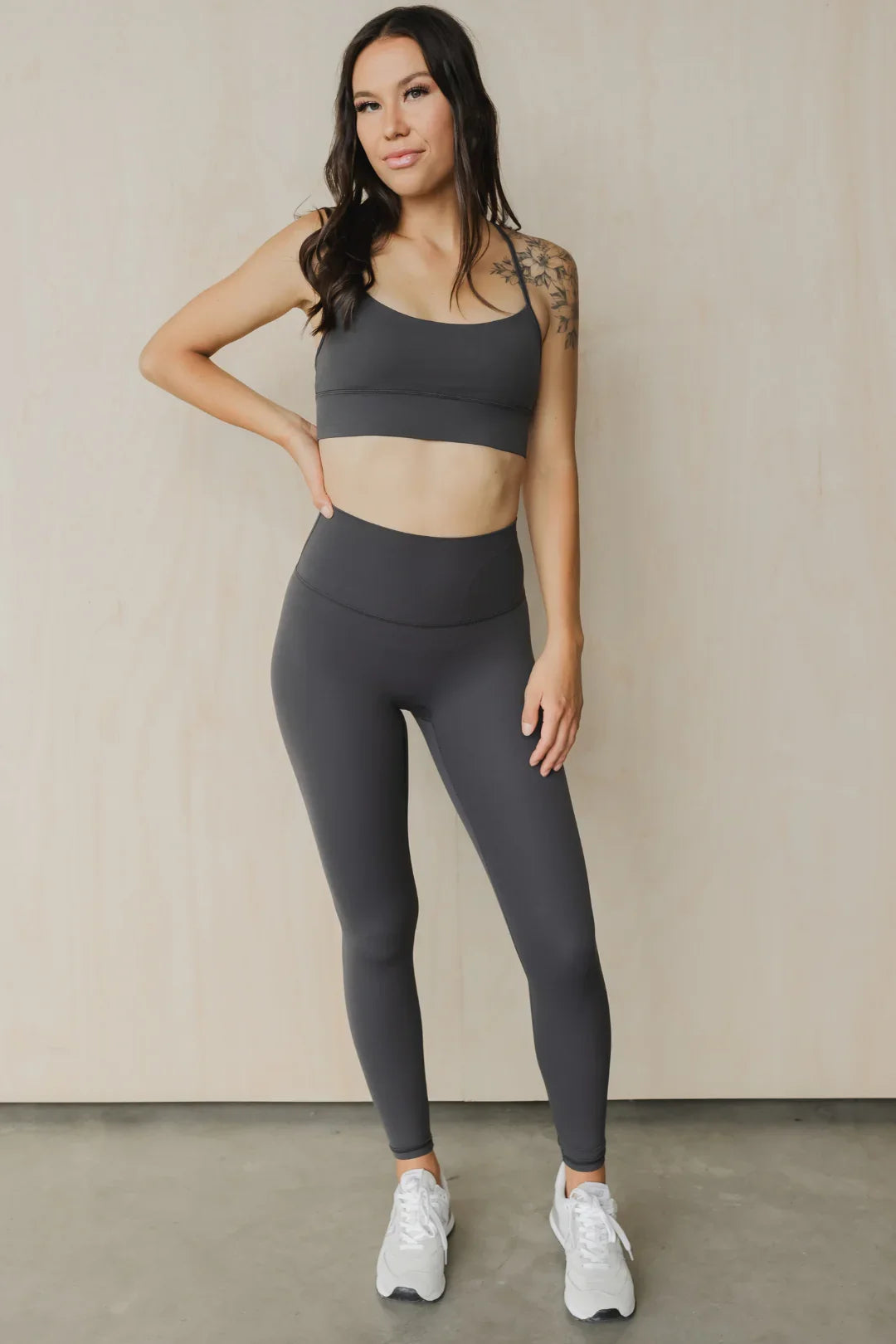 Woman in charcoal gray sports bra and leggings set, athletic wear, standing indoors