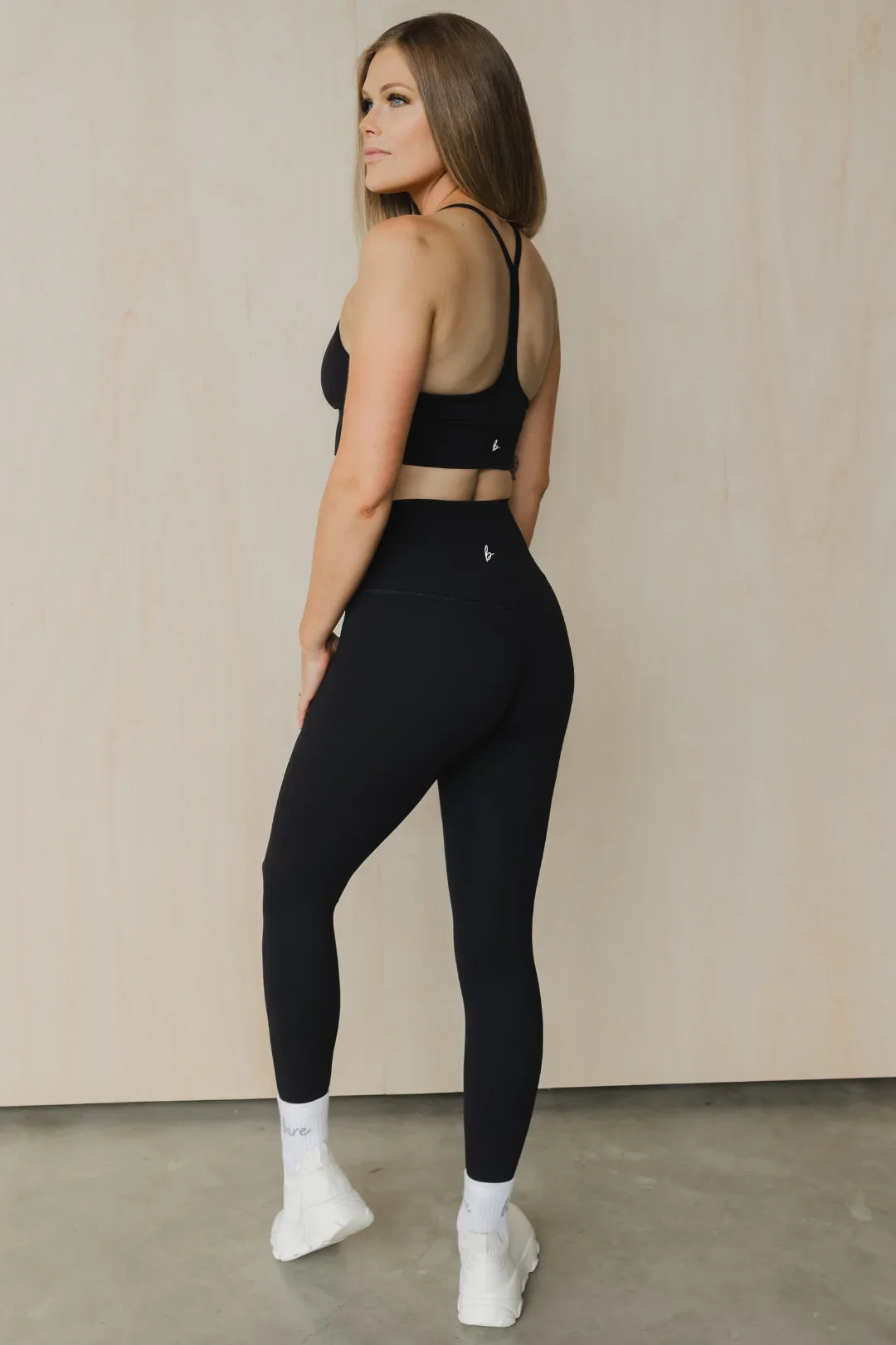 Woman modeling black athletic leggings and sports bra in studio with neutral background