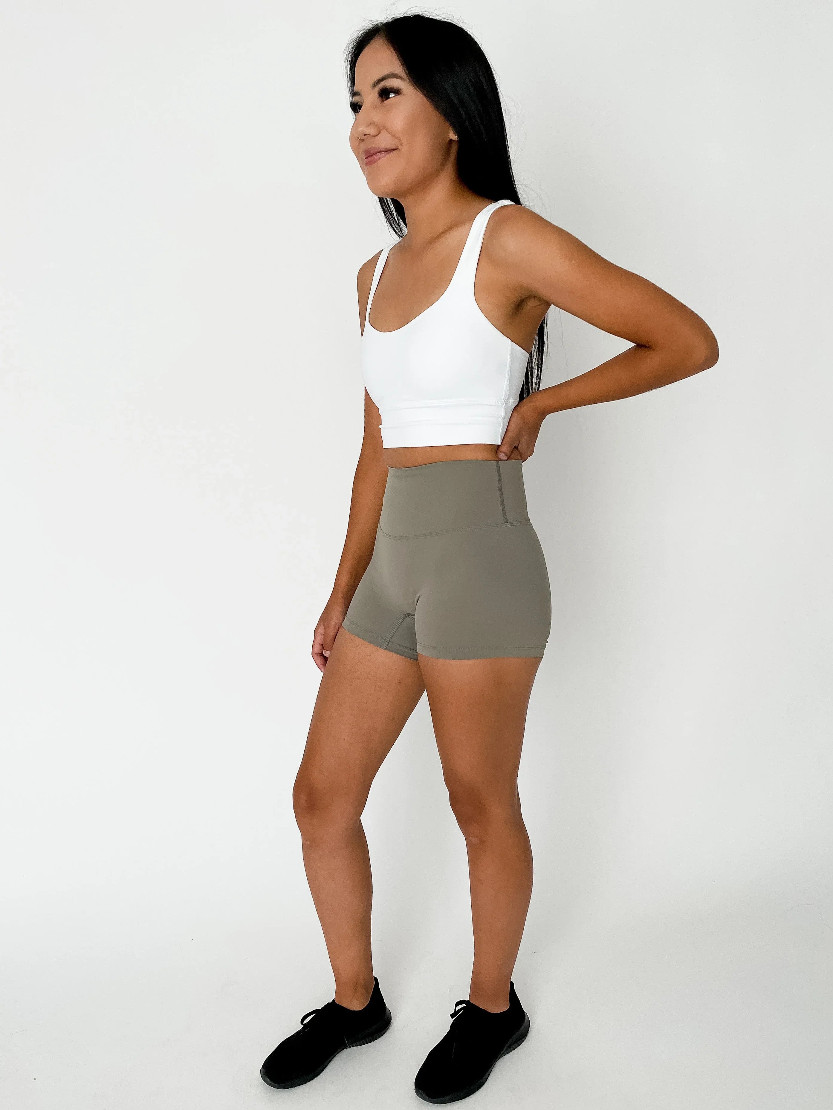 Woman in white sports bra and olive green biker shorts posing in studio