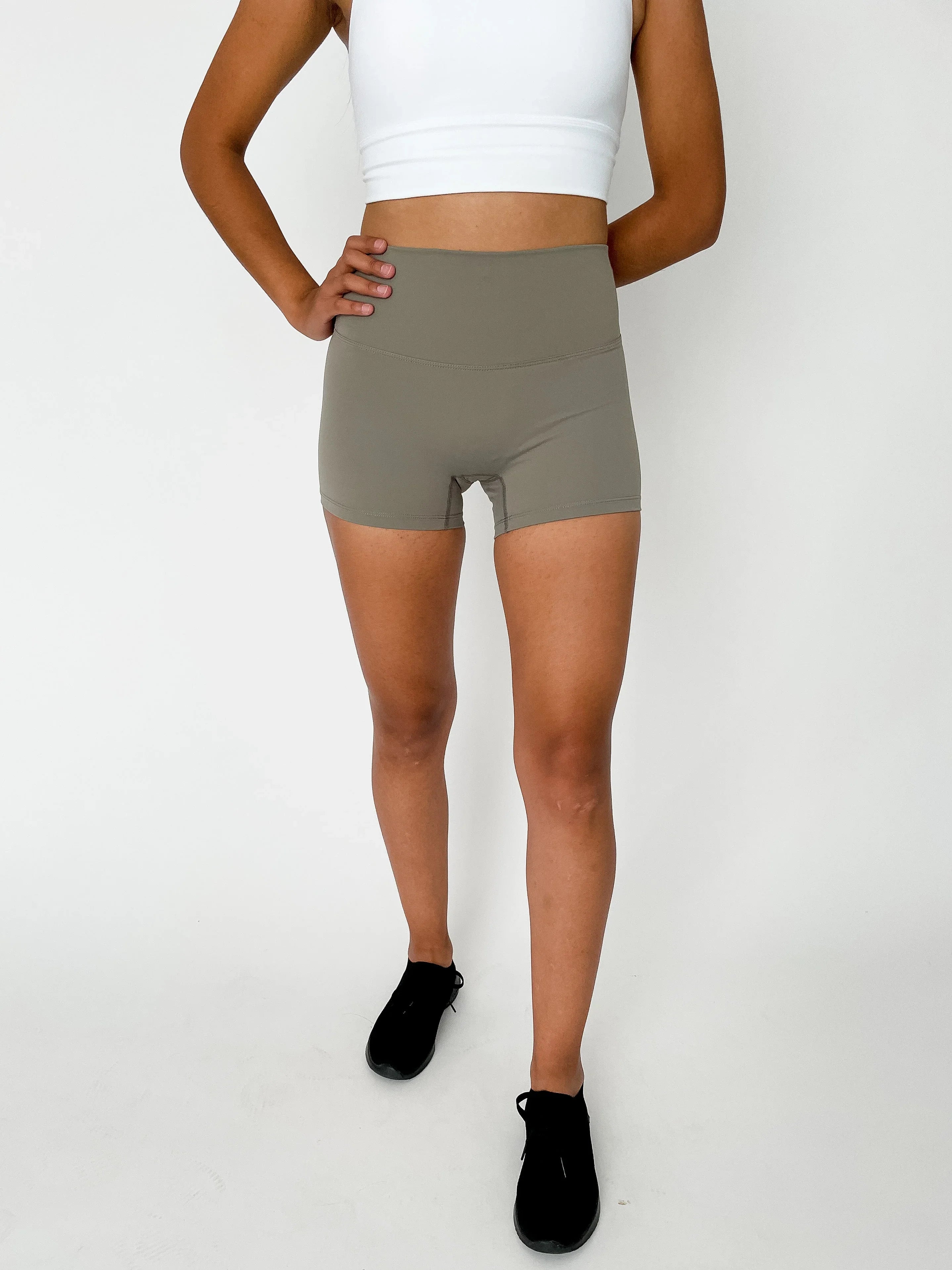 Woman in beige high-waisted workout shorts, white sports bra, and black sneakers