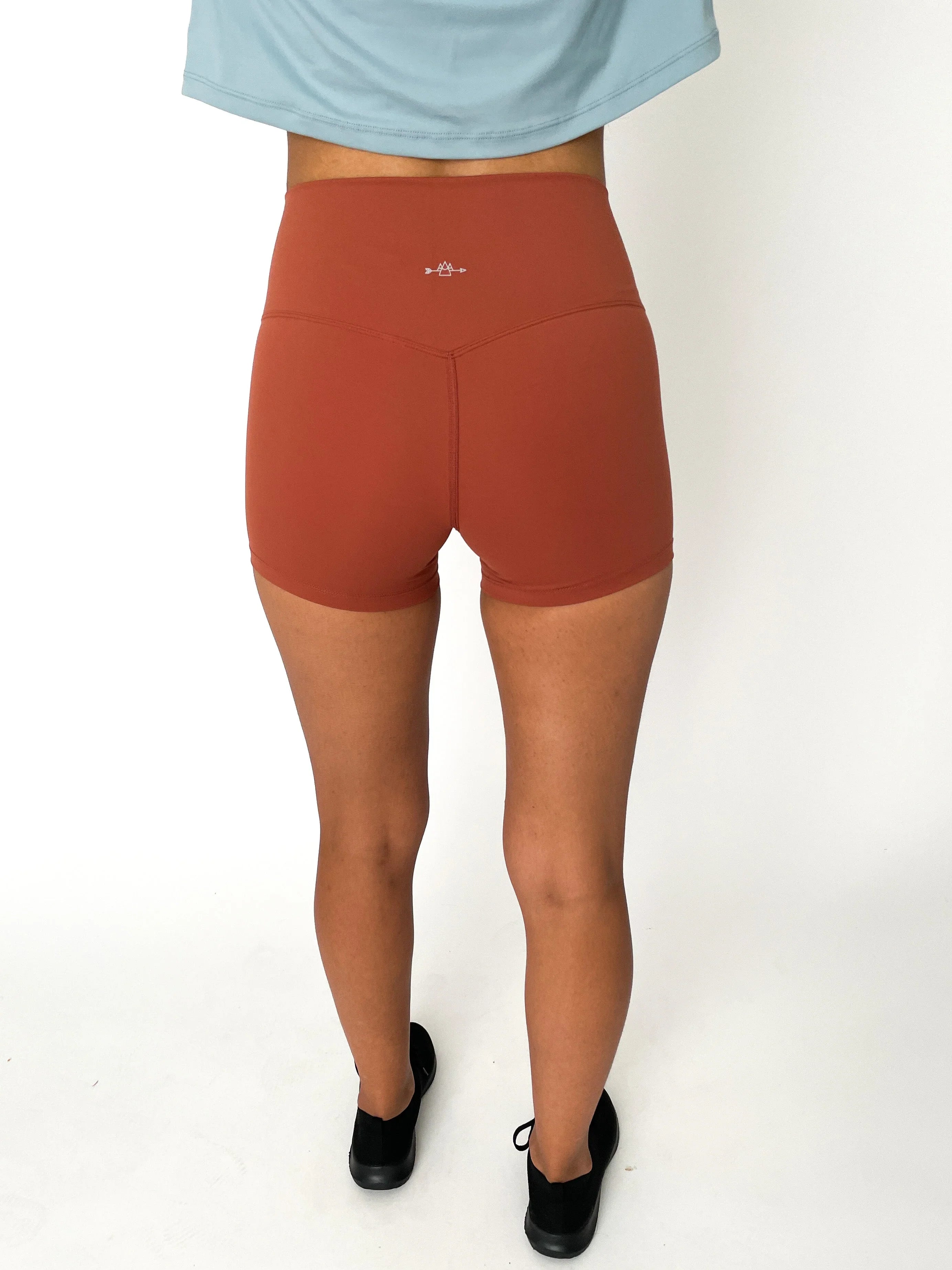 Back view of woman wearing rust orange high-waisted athletic shorts and black shoes