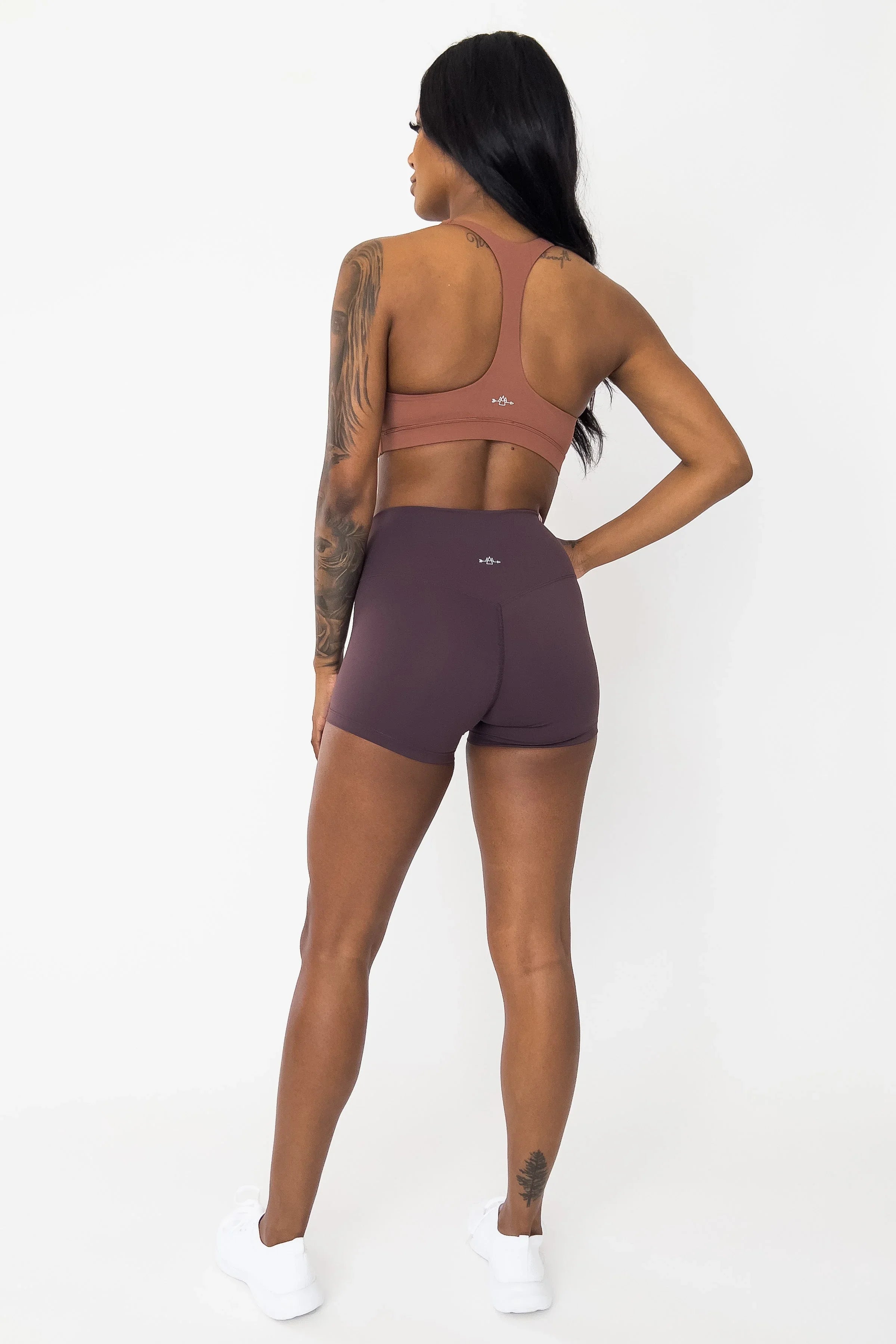 Woman in mauve sports bra and high-waisted gym shorts, showing back, athletic apparel