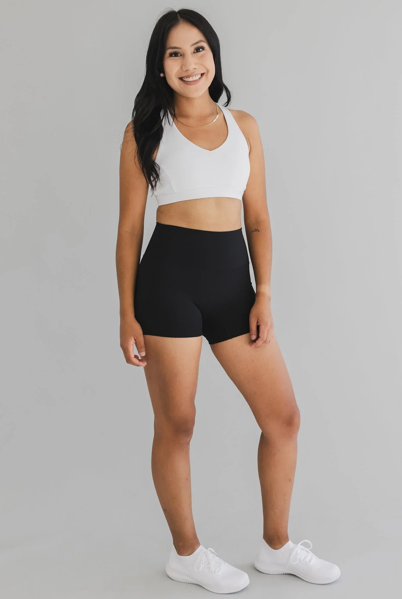 Woman in athletic wear modeling black high-waisted shorts and white sports bra