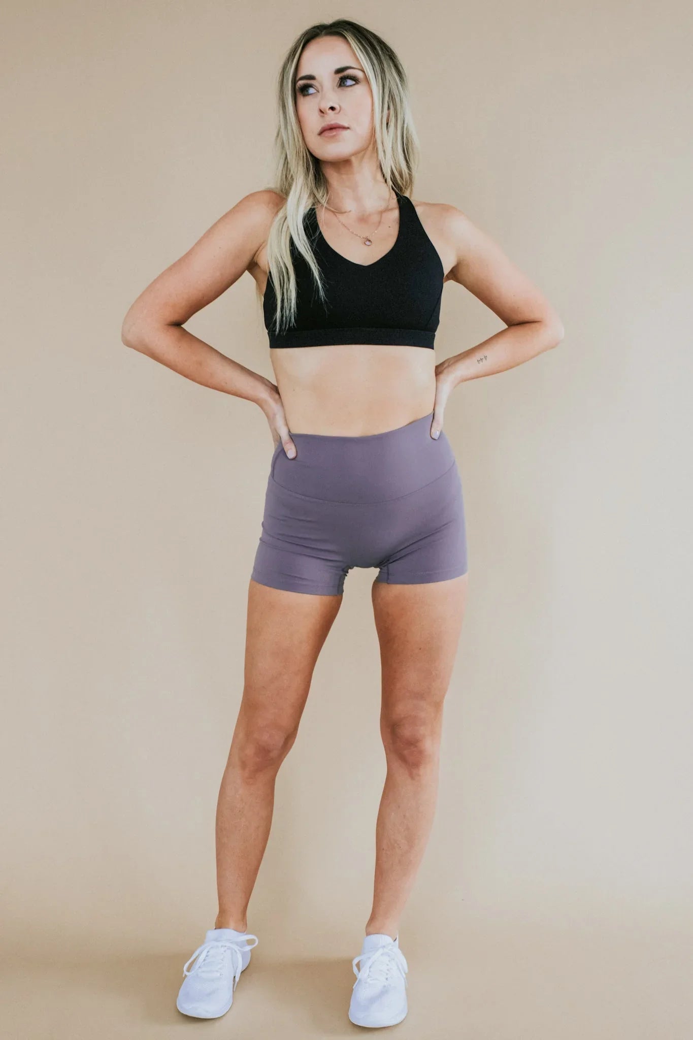 Woman in black sports bra and lavender athletic shorts, standing in studio, fitness apparel
