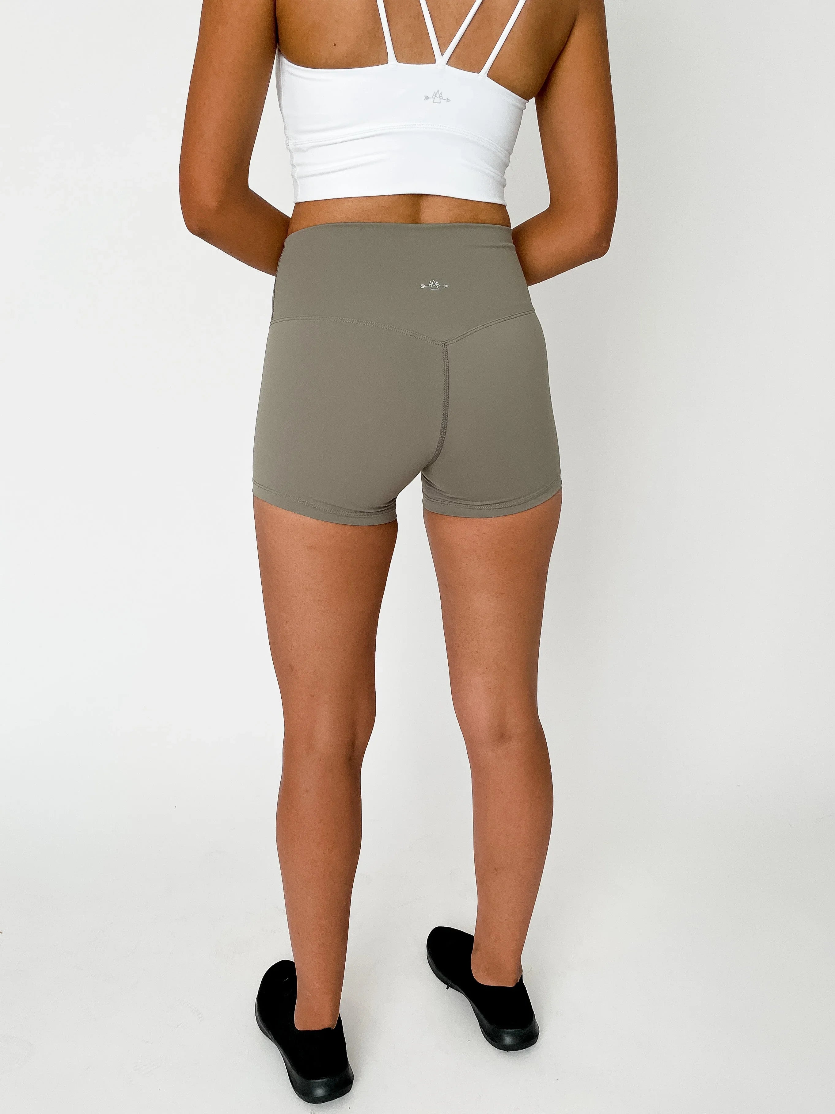 Woman in white sports bra and taupe athletic shorts, standing on white background