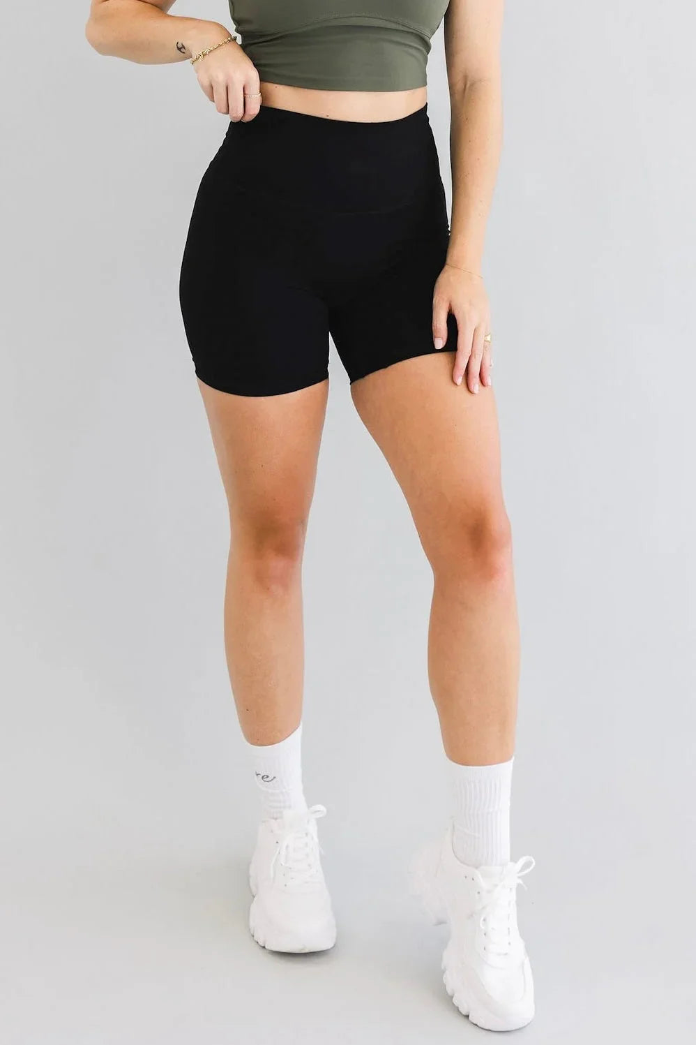 Woman wearing black high-waisted biker shorts, green crop top, white sneakers, fitness style
