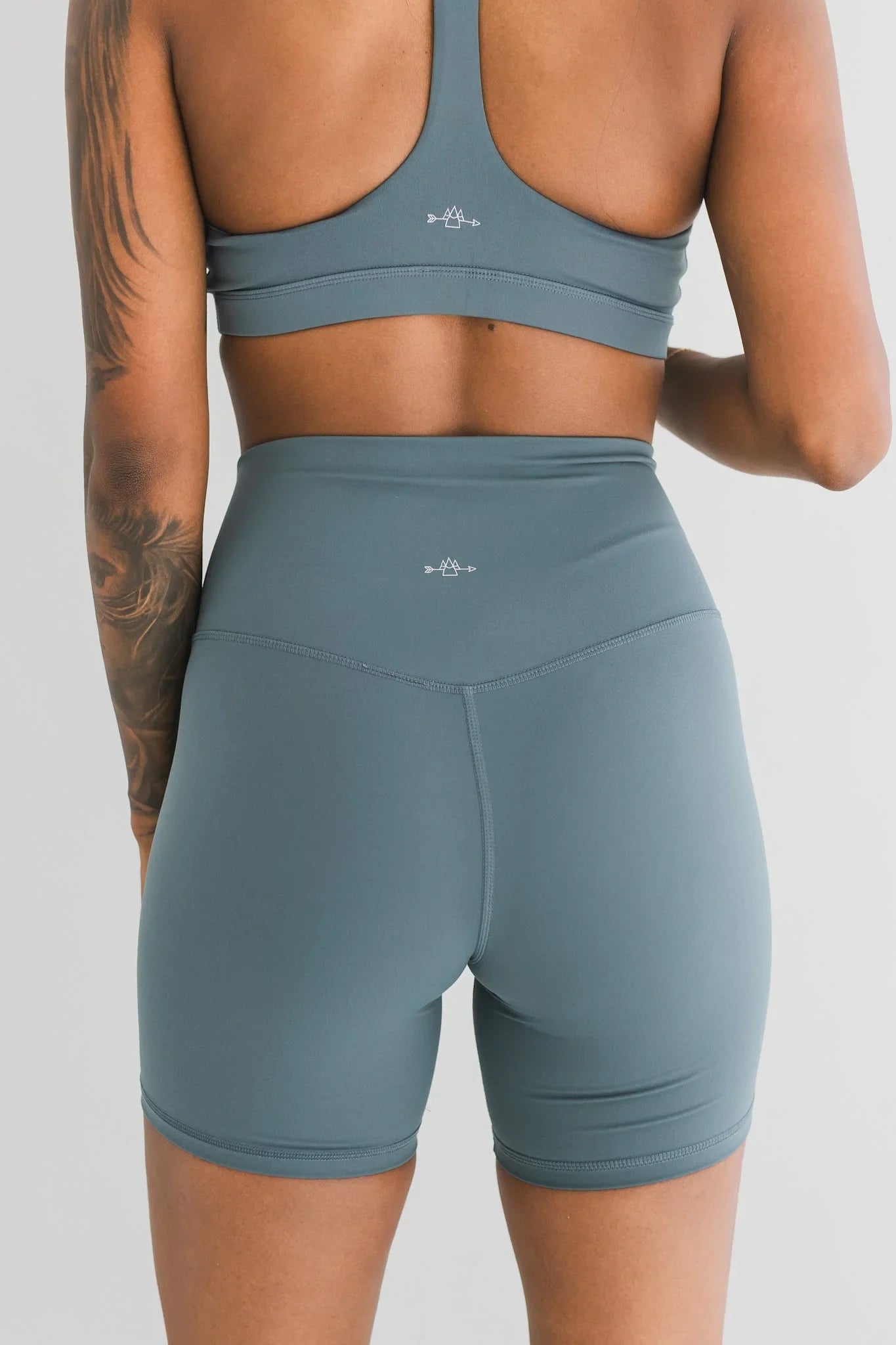 Woman wearing teal sports bra and high-waisted biker shorts, fitness apparel back view