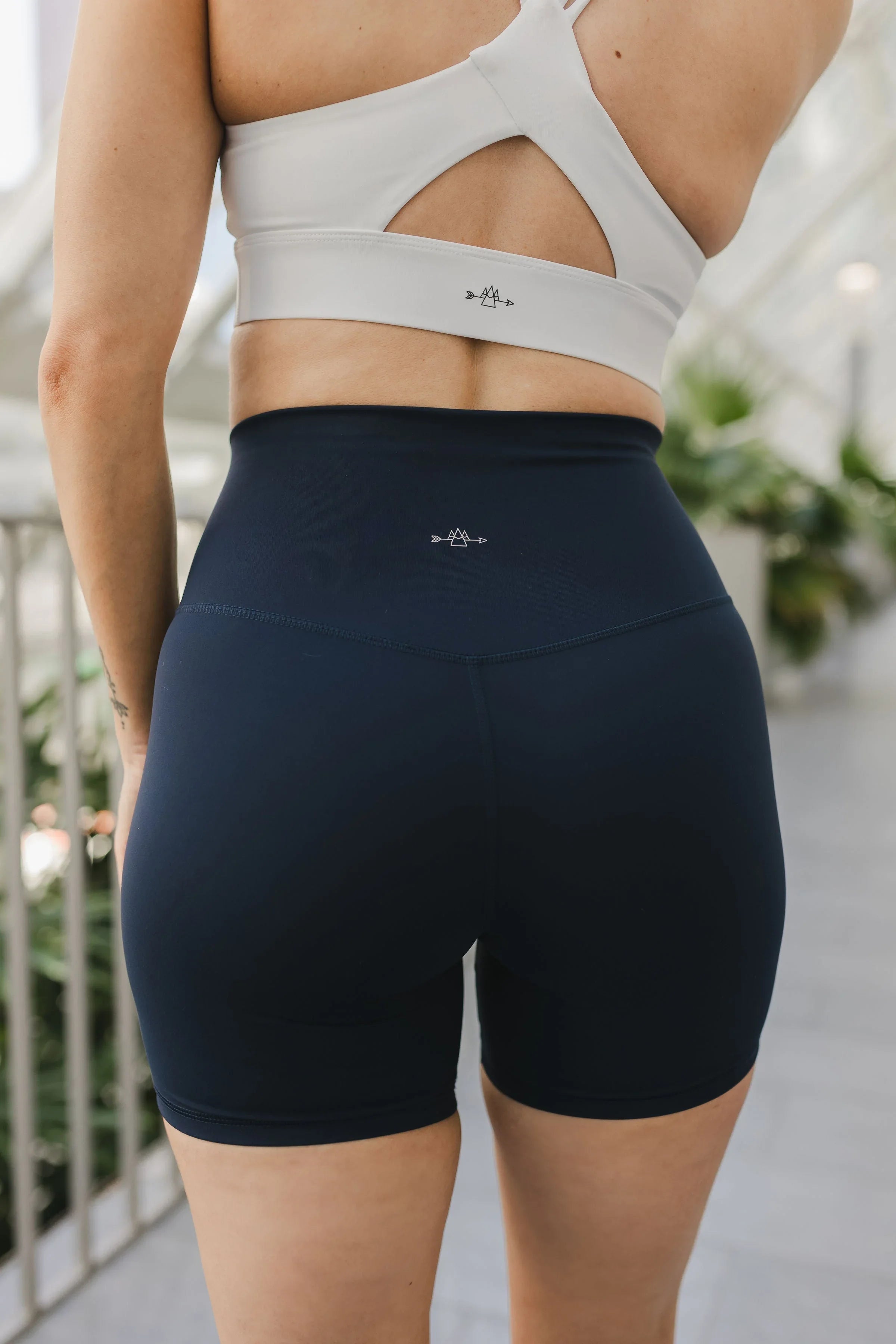 Woman wearing navy high-waisted bike shorts and white sports bra with cutout back detail