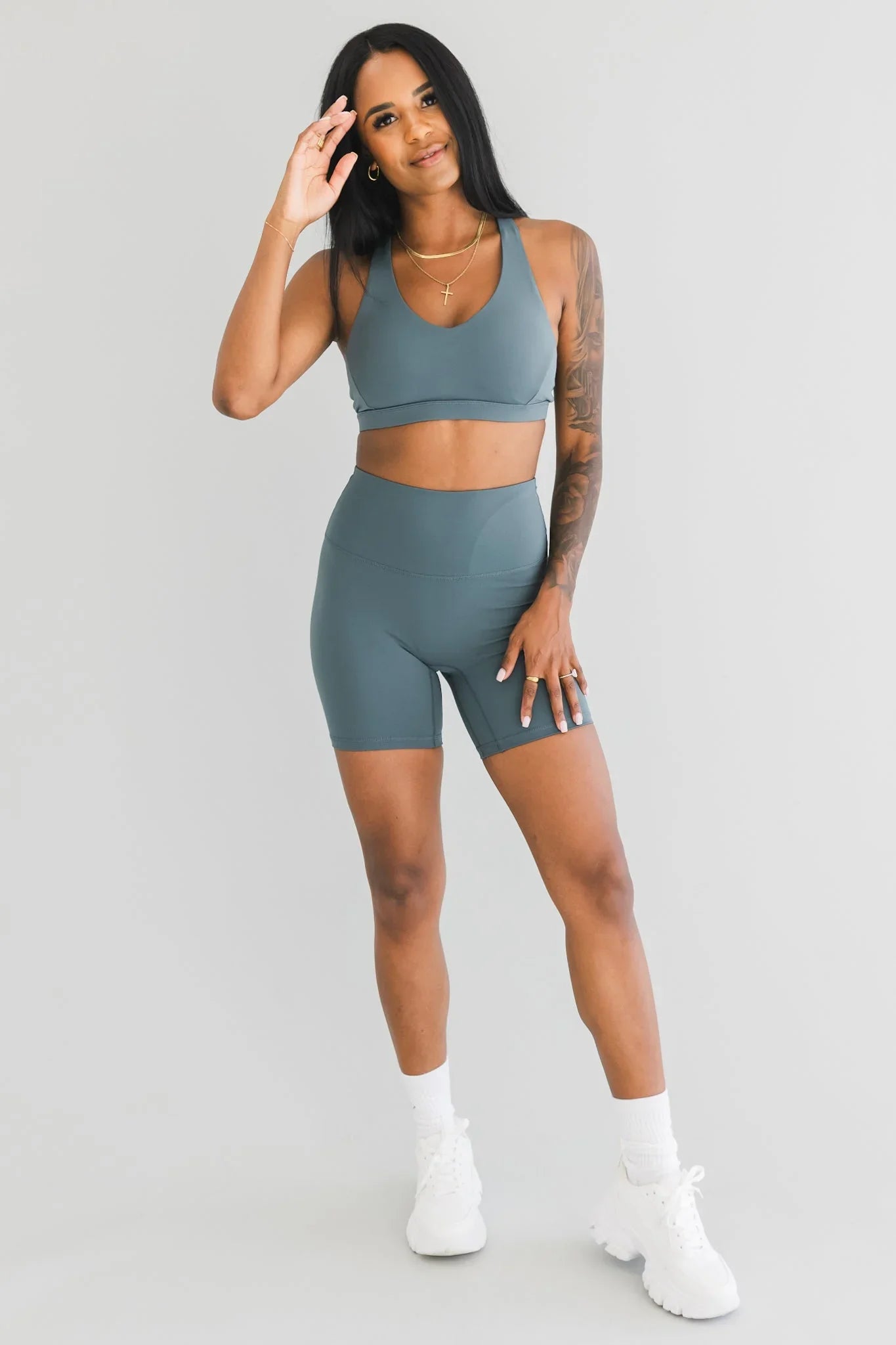 Woman in teal sports bra and biker shorts set, posing on white background, athletic wear fashion.