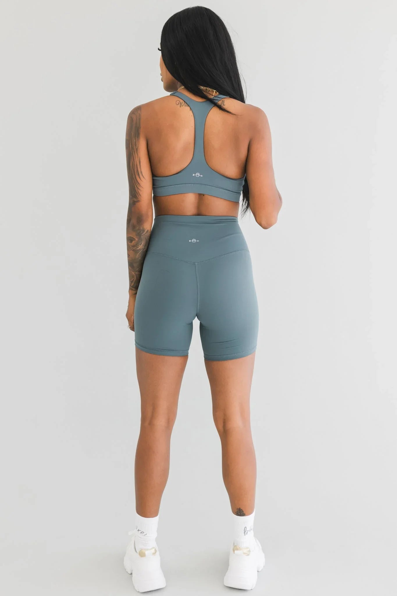 Woman modeling teal gym shorts and sports bra set, back view, on white background