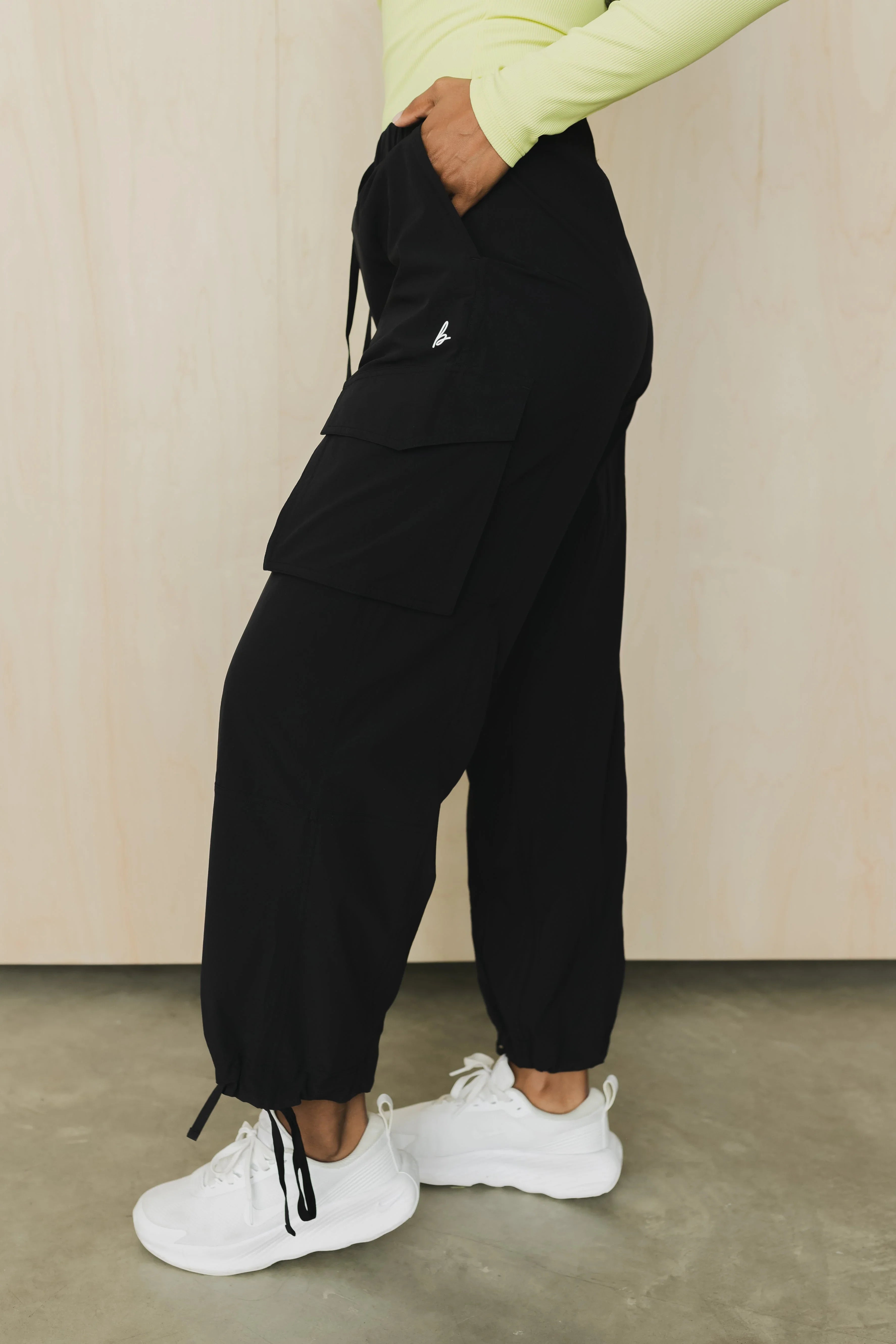 Black cargo jogger pants with side pocket, drawstring cuffs, white sneakers, light top.
