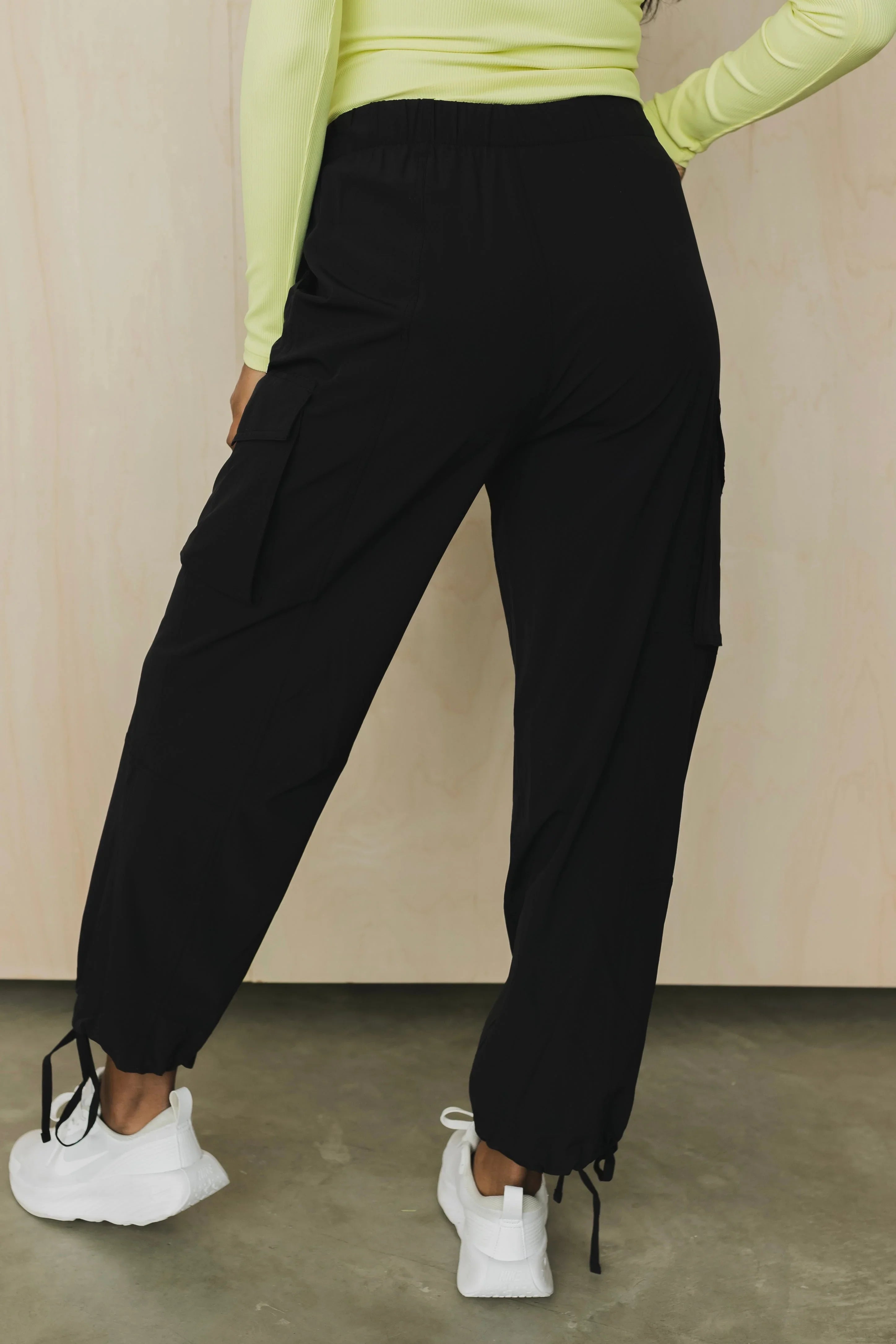 Back view of black cargo jogger pants with drawstring cuffs and white sneakers