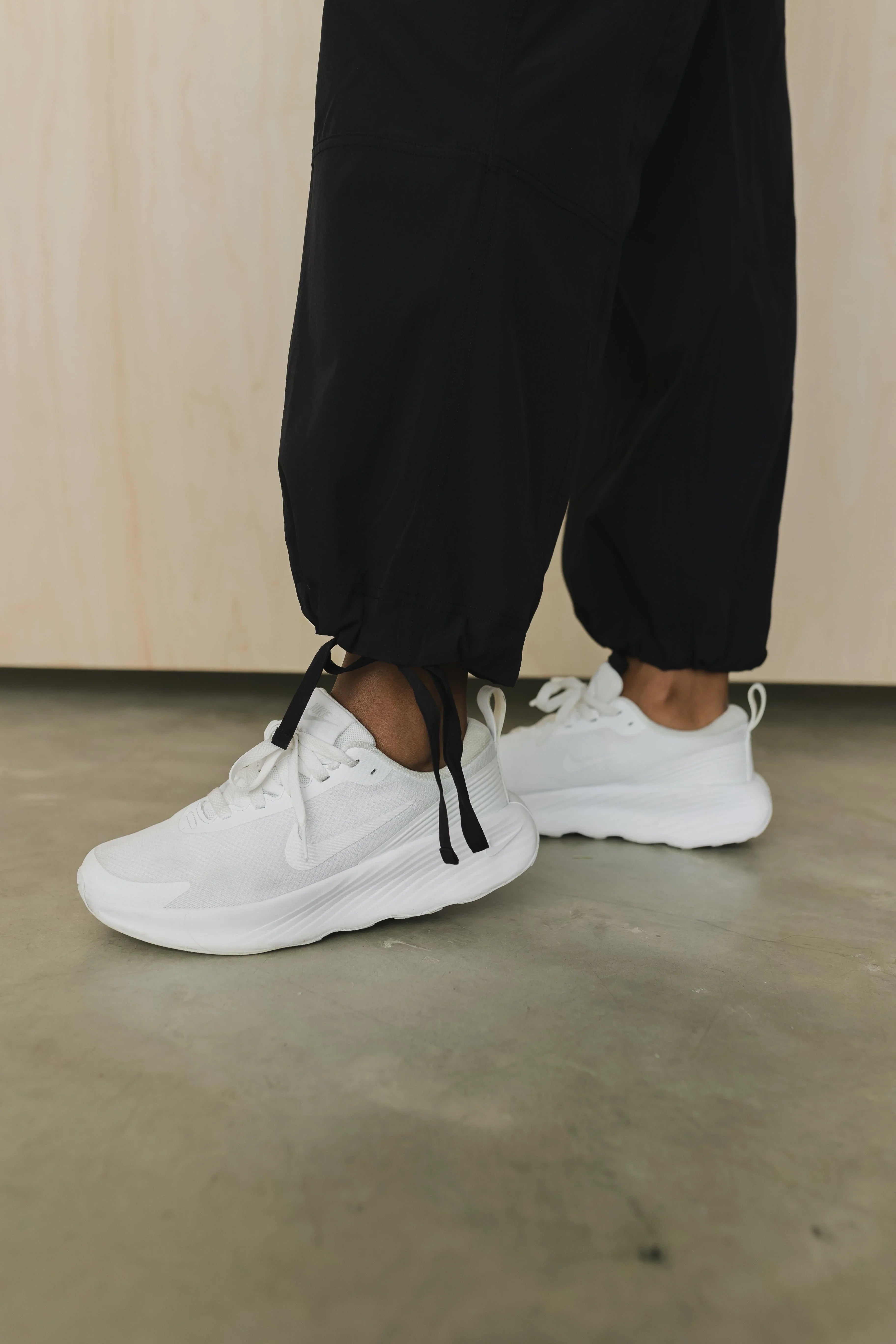 White sneakers with black drawstring joggers on concrete floor
