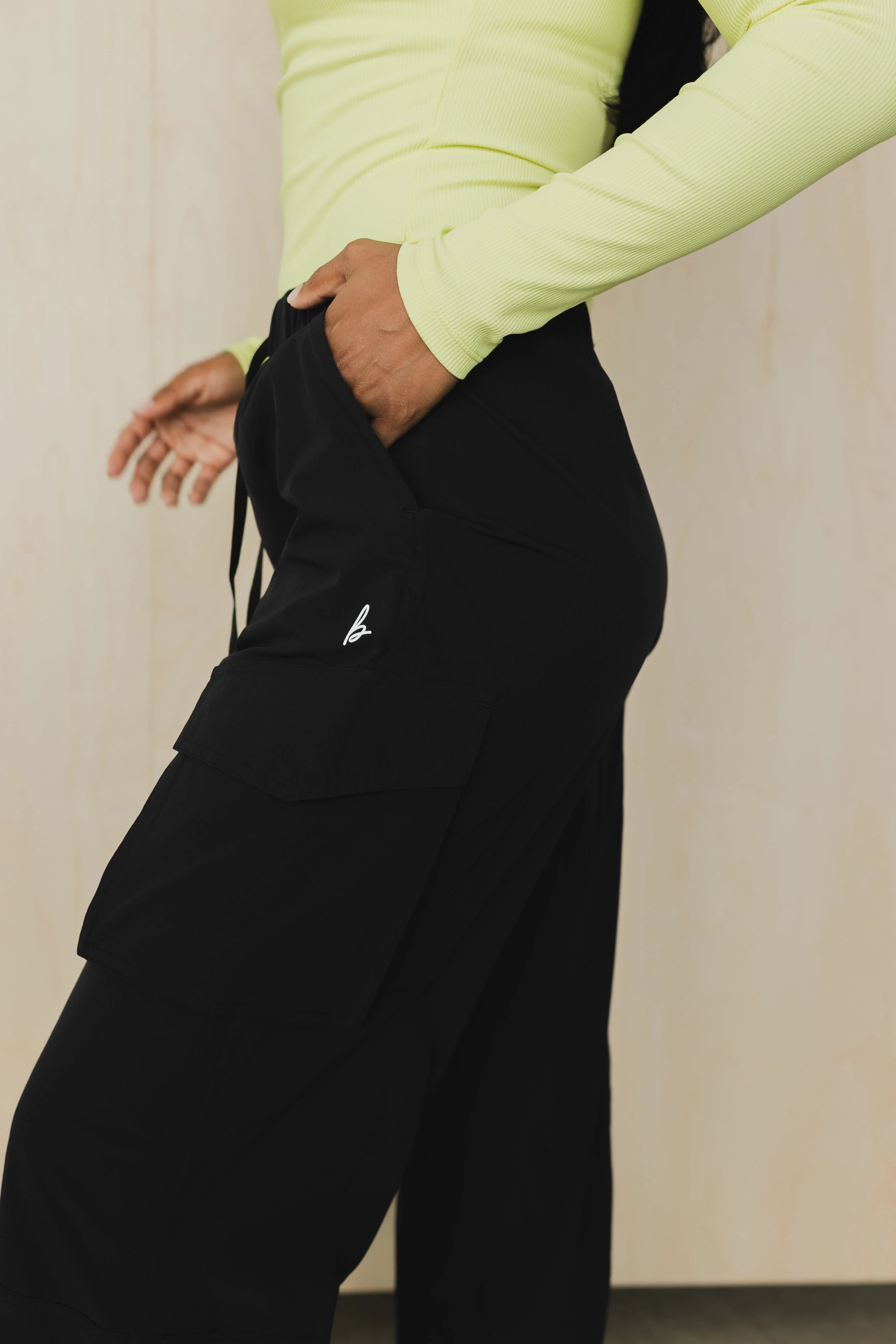 Woman in neon long sleeve top wearing black cargo pants with hand in pocket