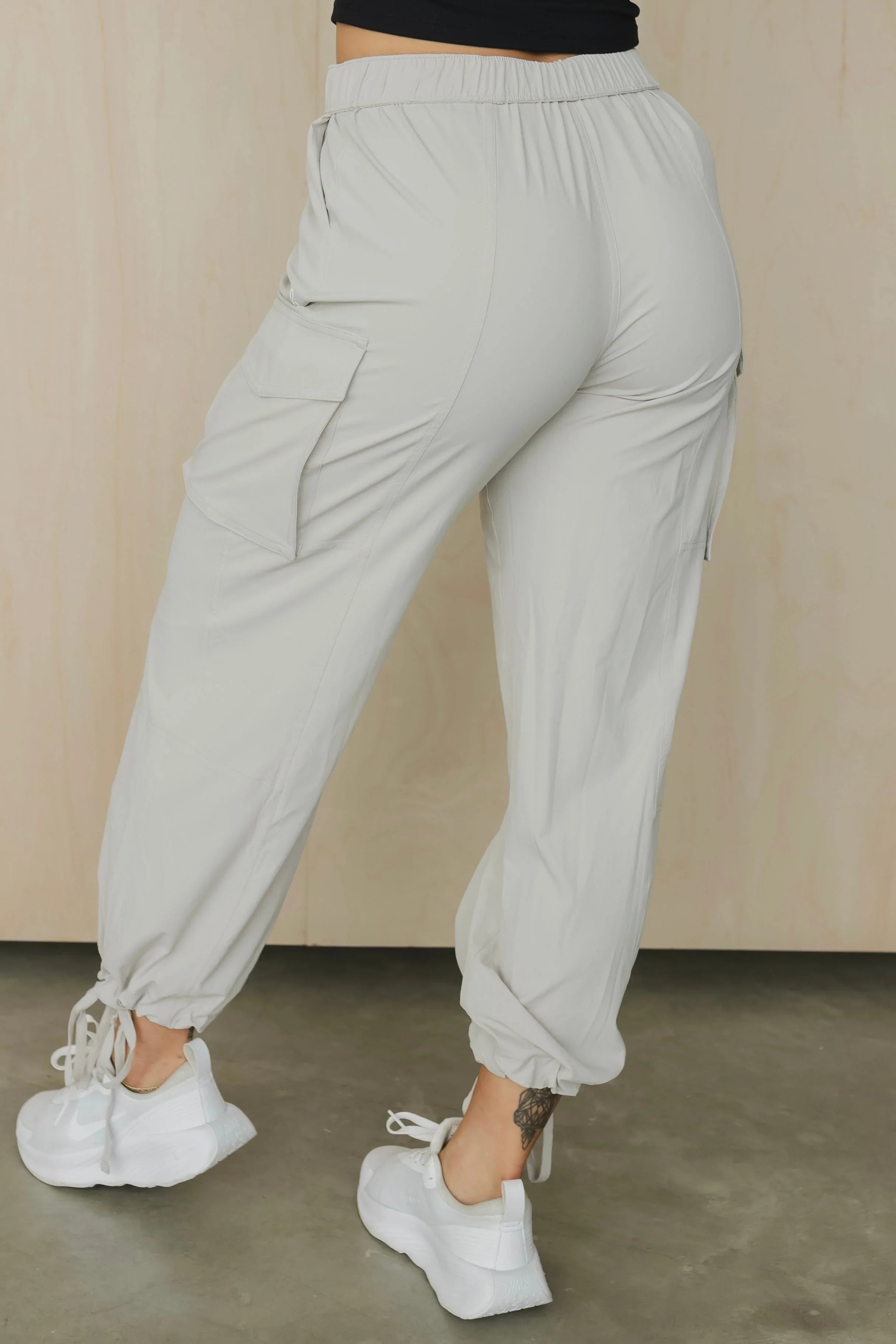 Back view of light gray cargo jogger pants with side pockets, white sneakers, and ankle tattoo