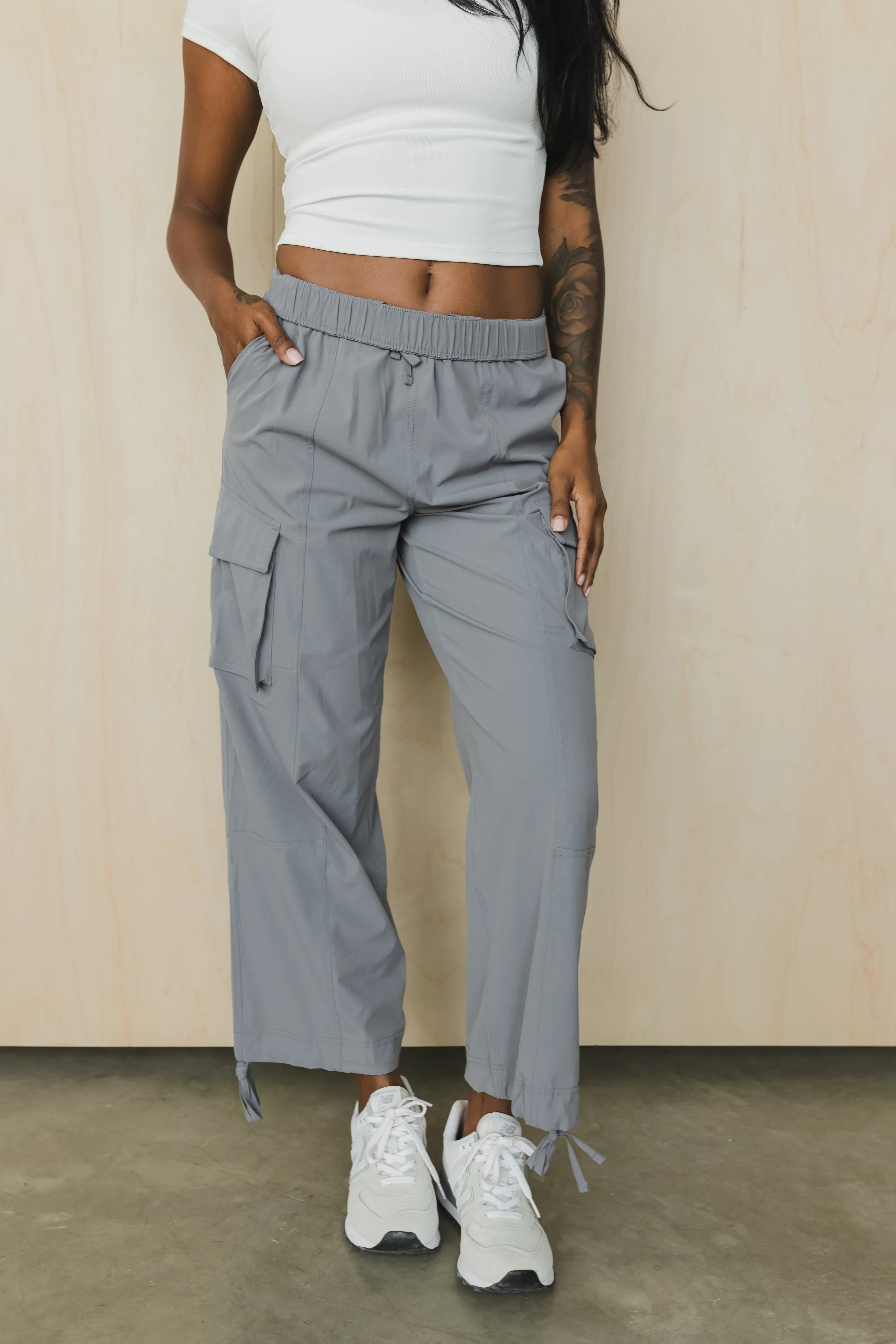 Woman wearing gray cargo pants, white crop top, and white sneakers on concrete floor