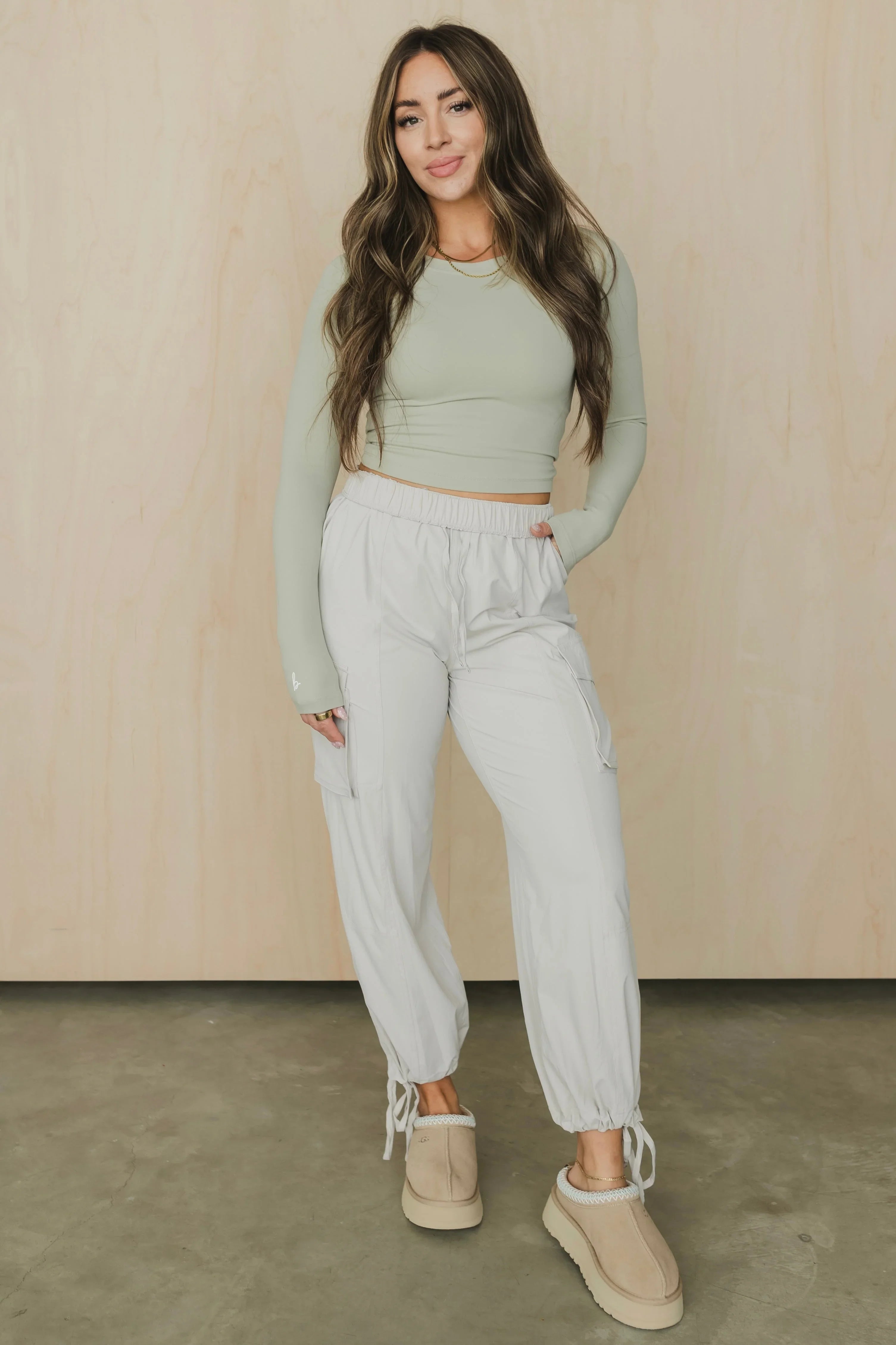 Woman in sage green crop top, white jogger pants, and beige platform slippers standing indoors