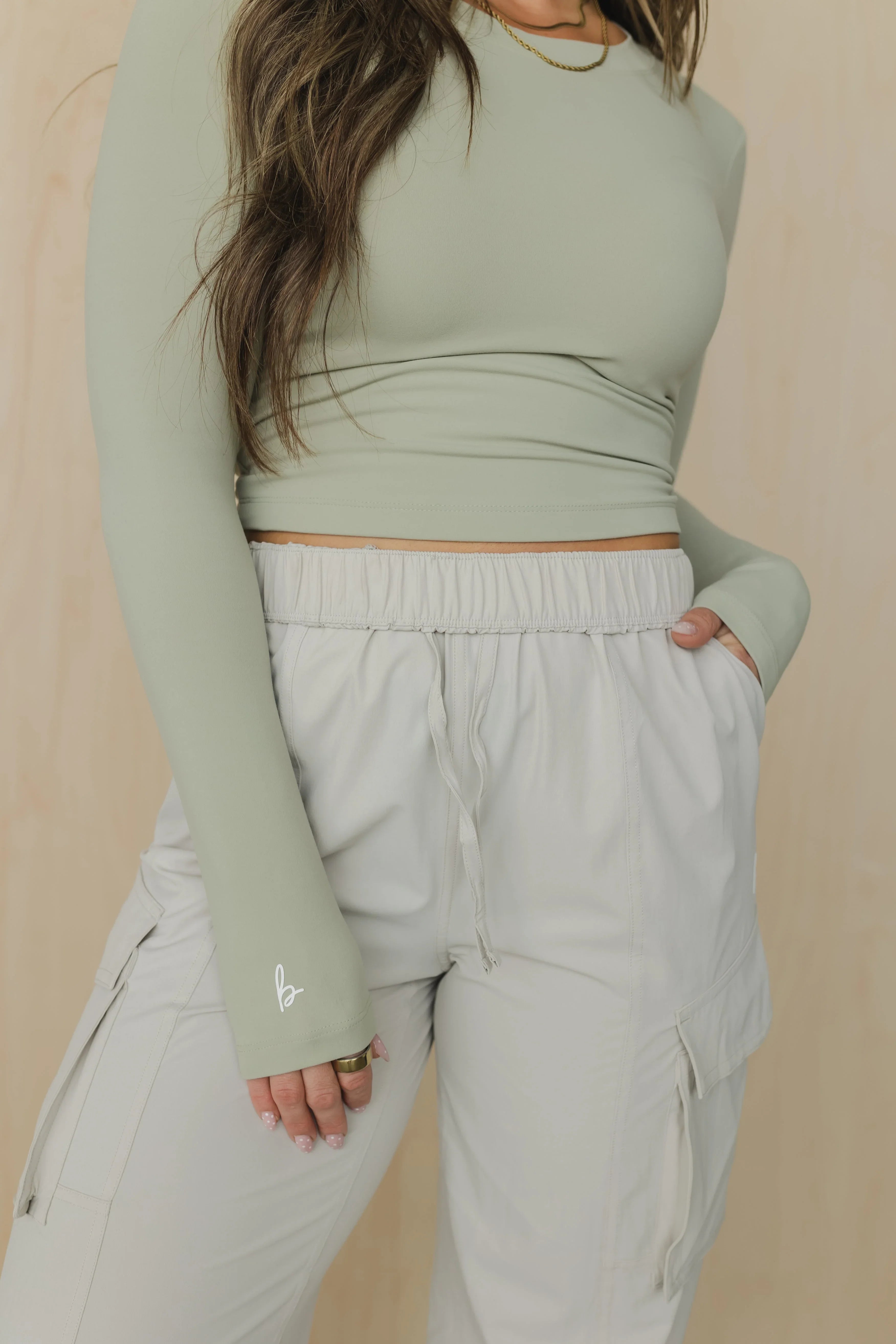 Woman in sage green long sleeve crop top and light cargo pants with drawstring waist