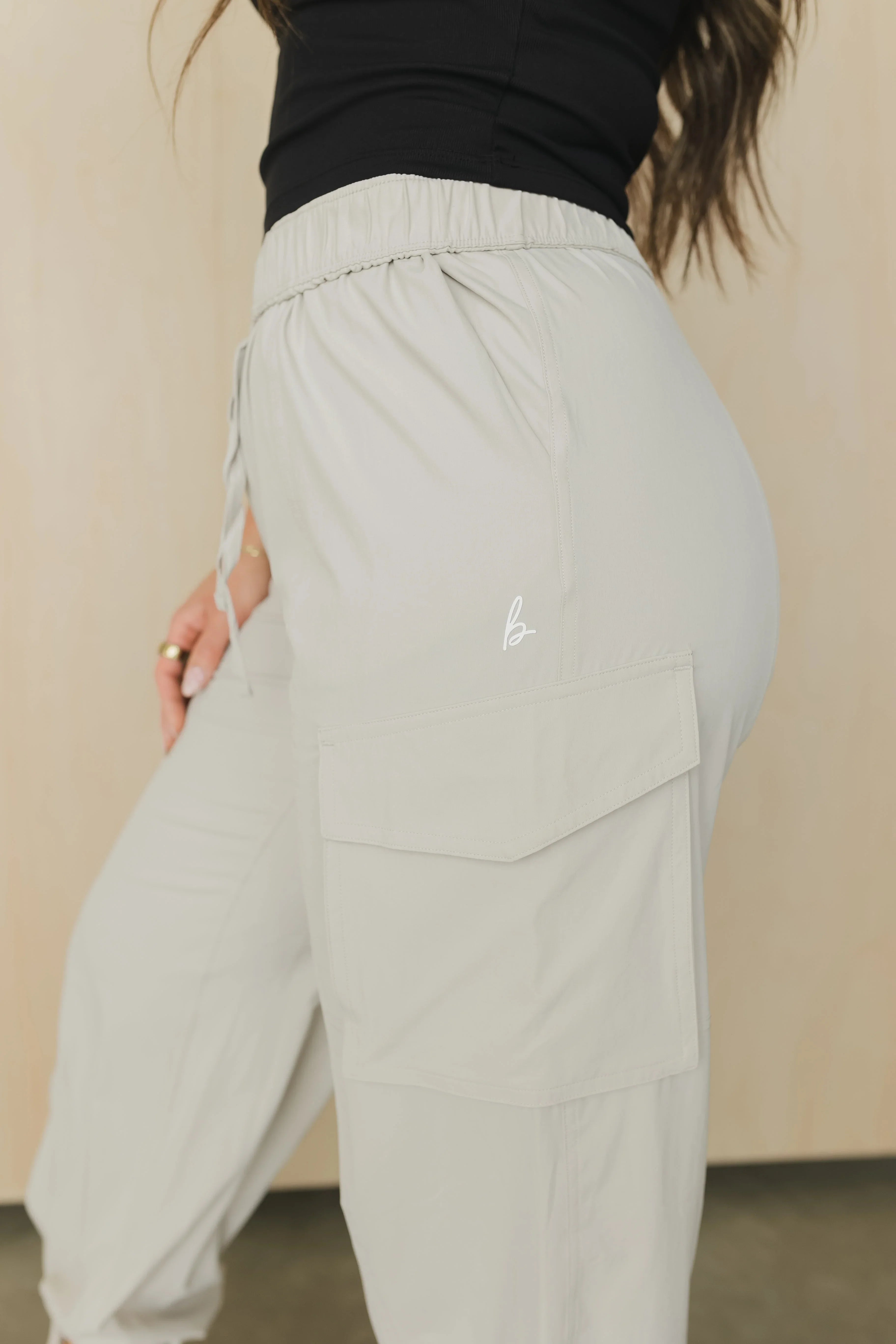 Light gray cargo pants with side pocket and elastic waist, woman wearing black top