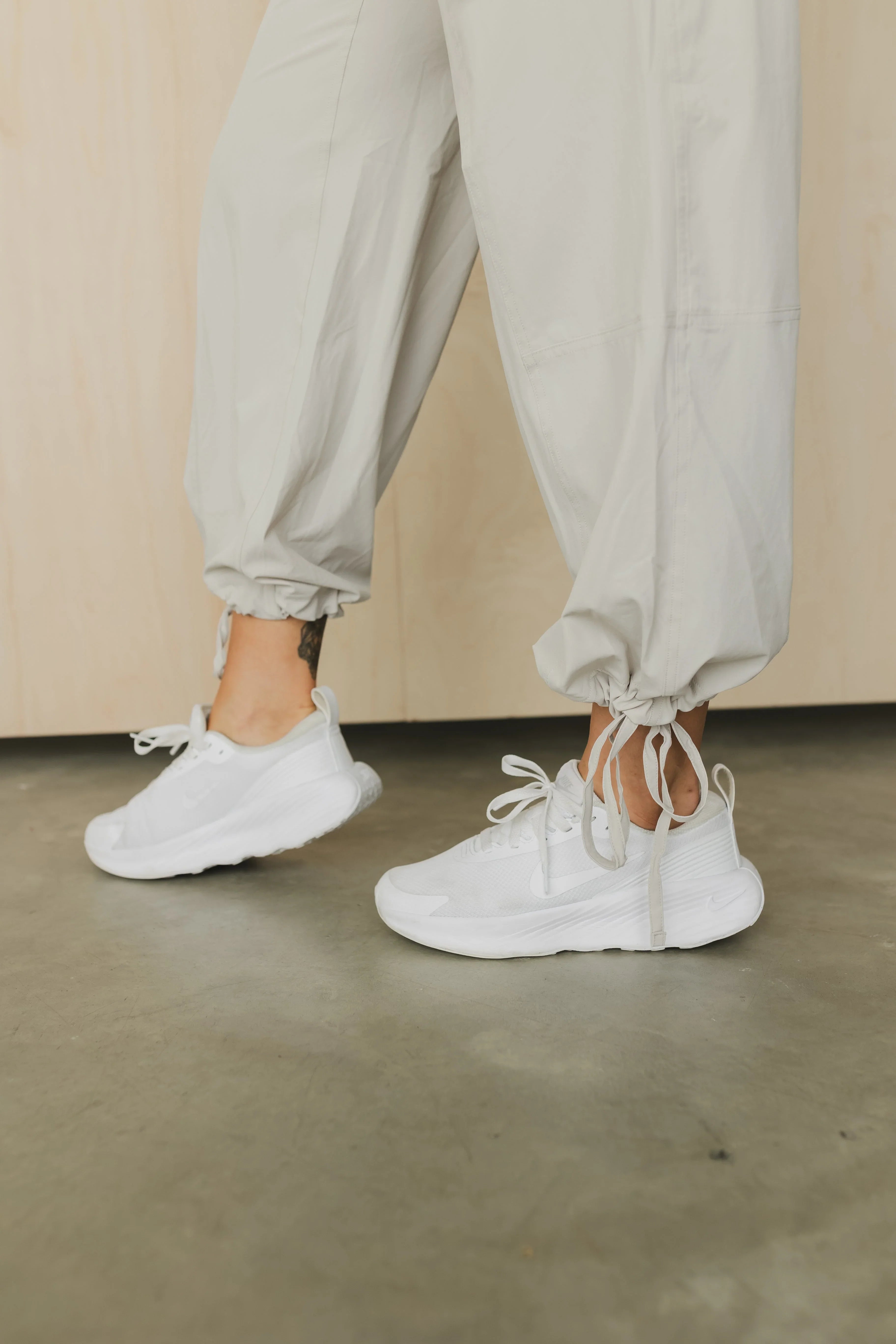 White Nike sneakers with drawstring cuff pants on a concrete floor