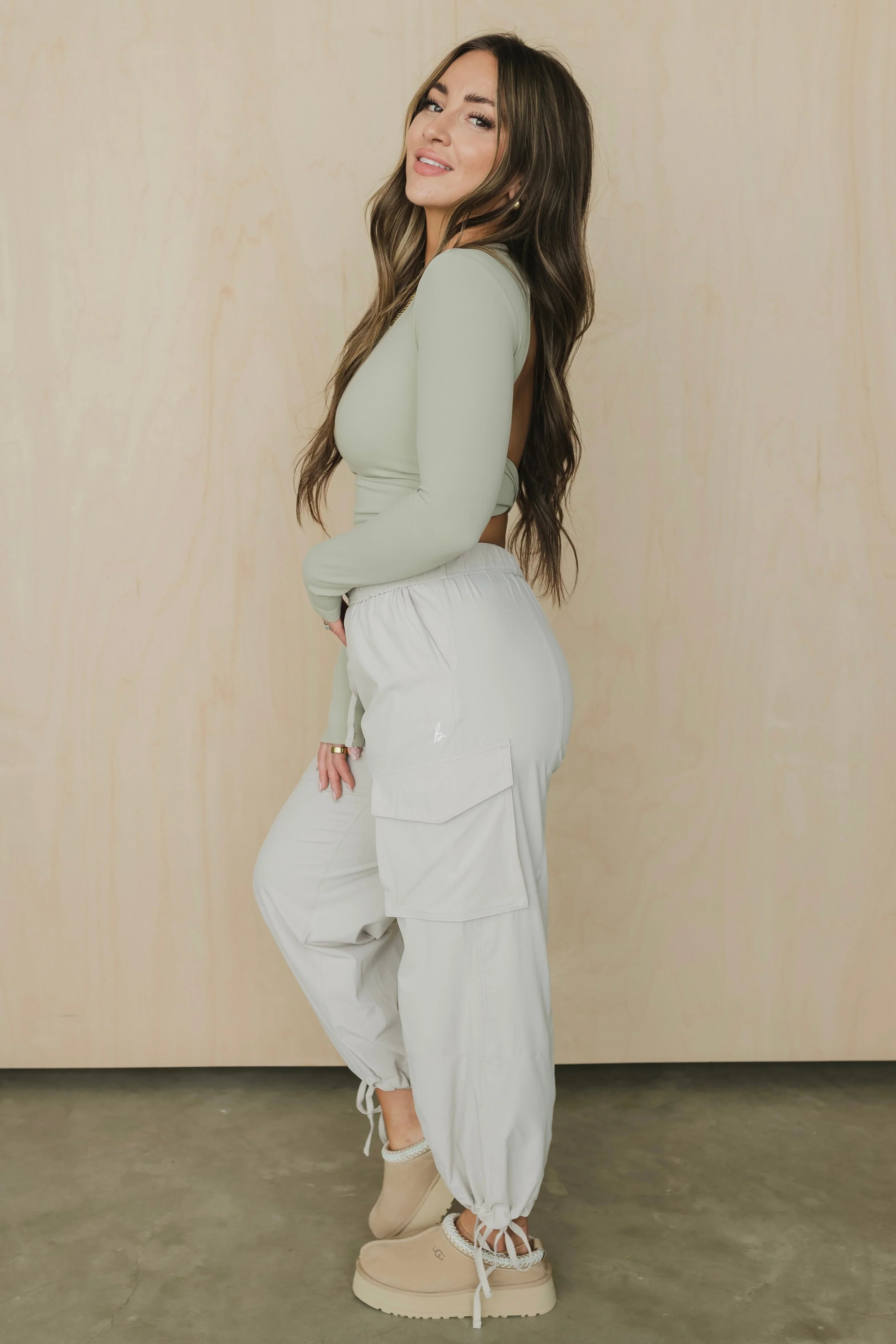 Woman in sage green open-back top and light cargo joggers, beige platform slippers