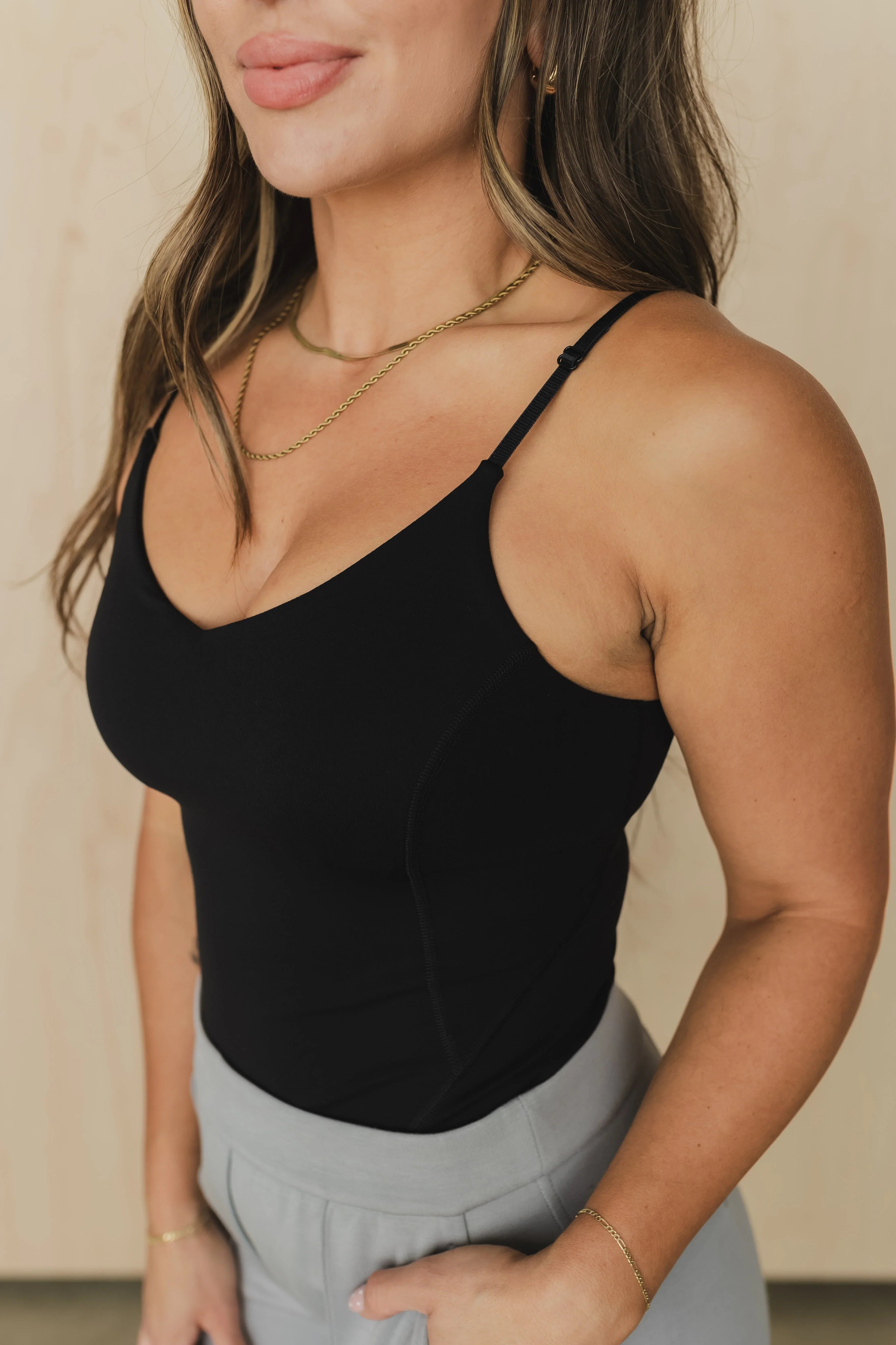 Woman in black camisole tank top, gray pants, gold necklaces, and wavy hair