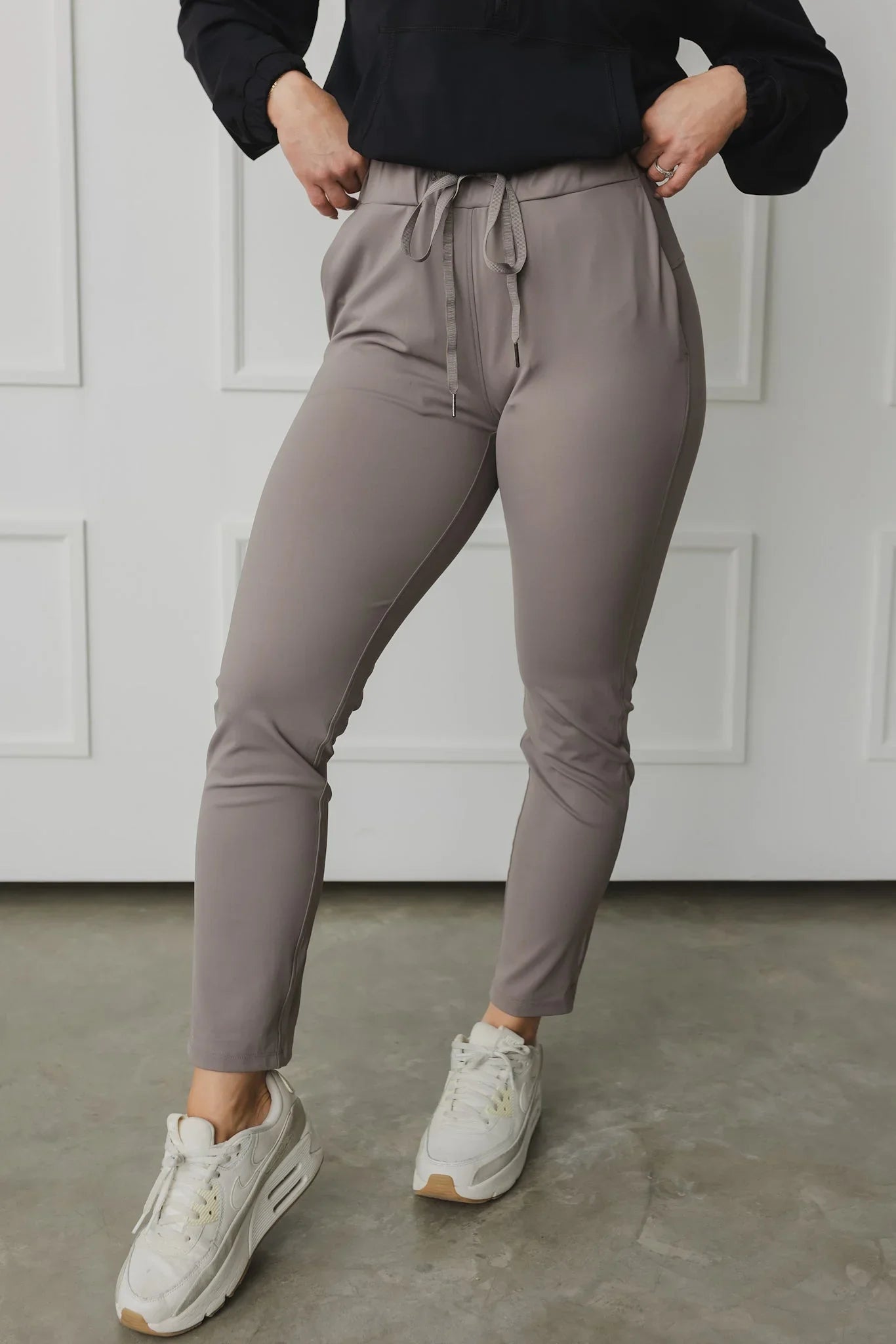 Woman wearing taupe jogger pants with drawstring waist and white sneakers, indoor setting