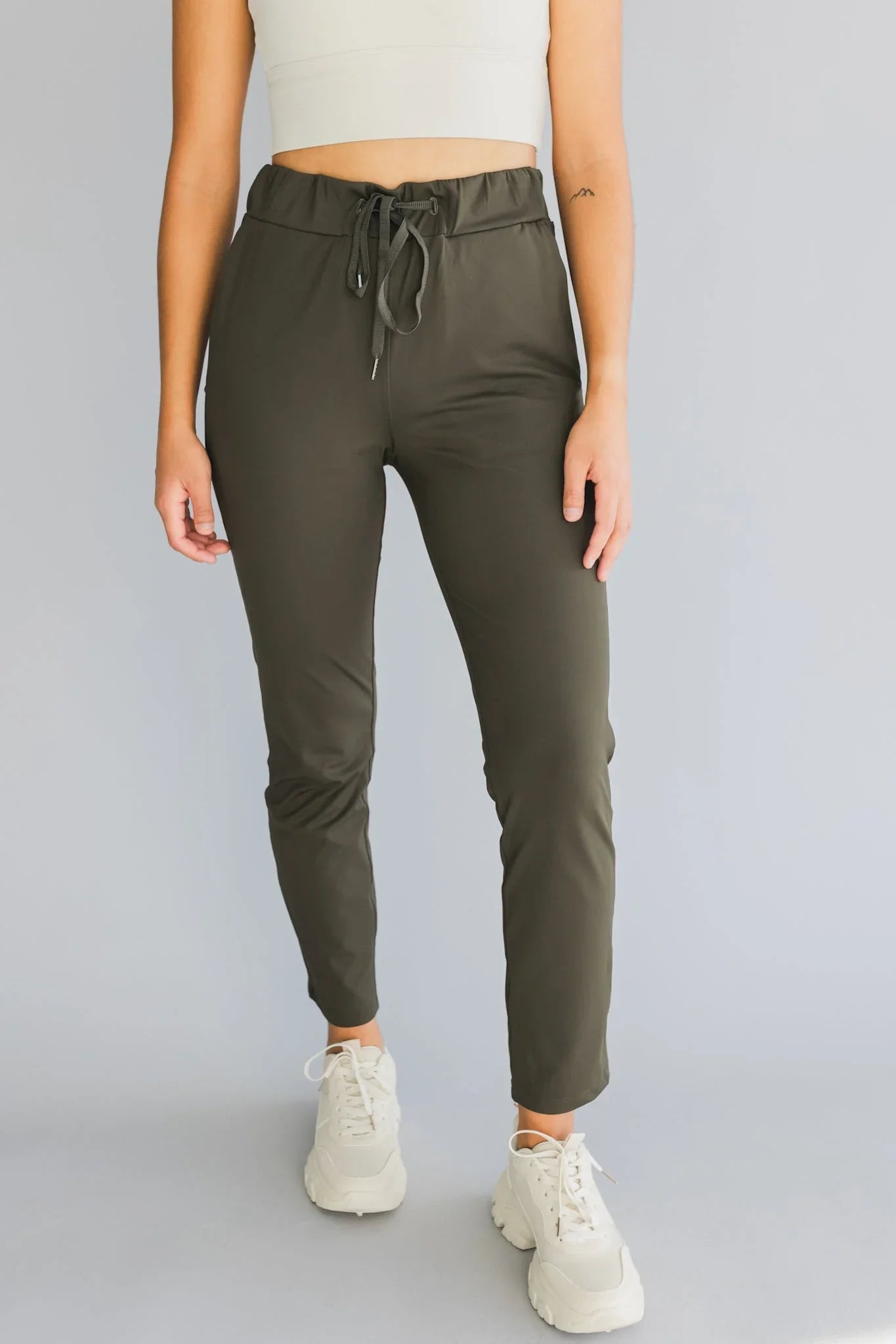 Woman wearing olive green jogger pants with drawstring waist and white sneakers