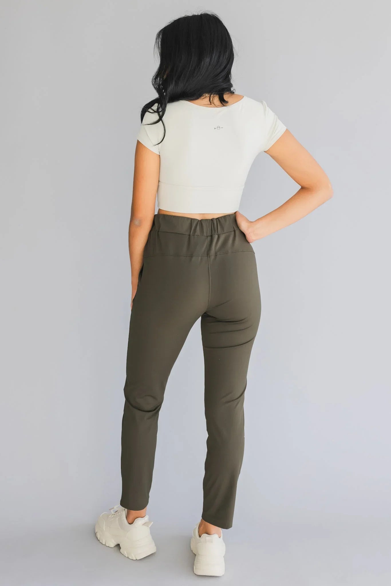 Woman wearing olive green high-waist pants, white crop top, and chunky sneakers